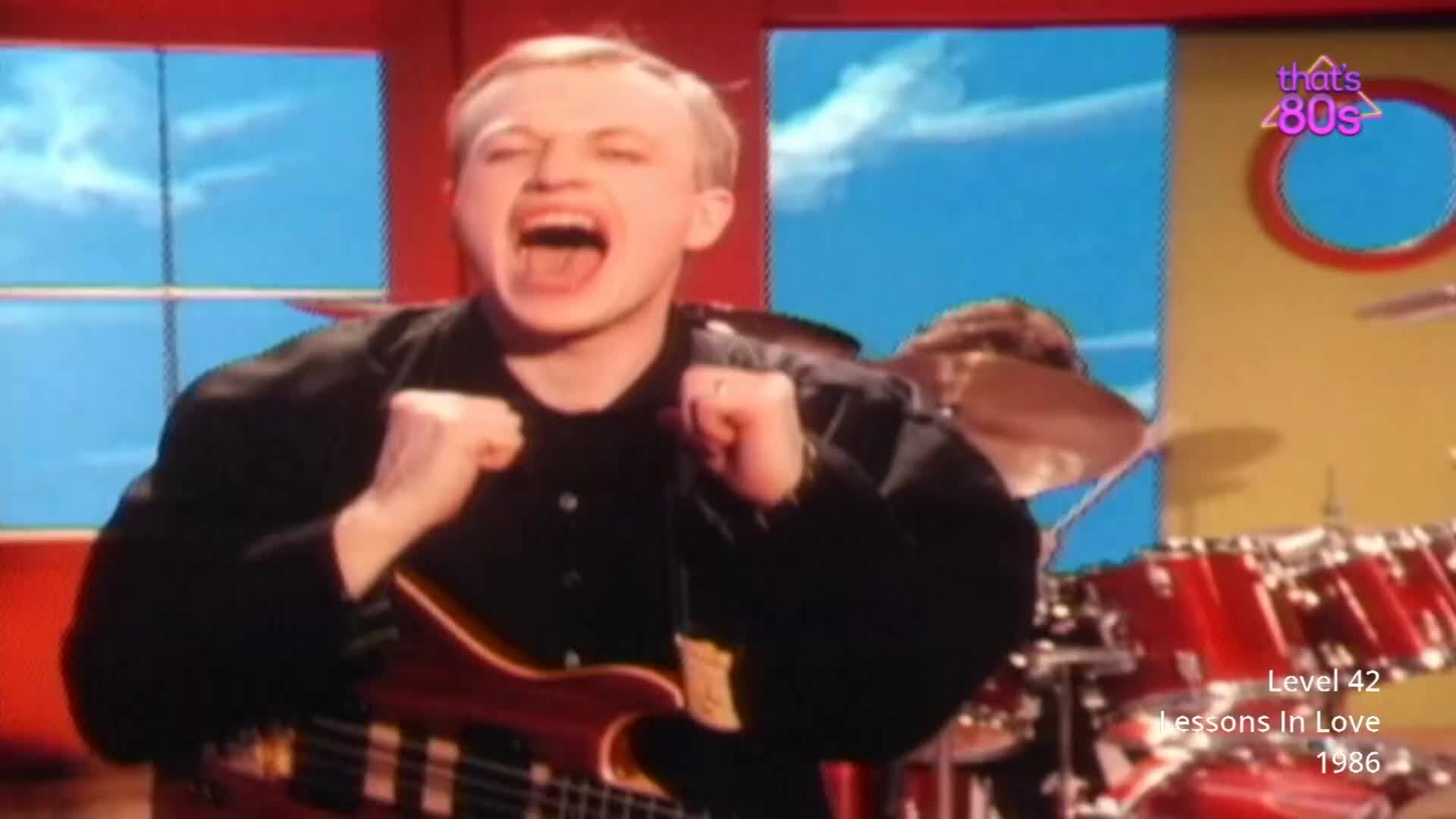 The lead singer belts out the lyrics, his fists clenched in excitement. Behind him, a drummer pounds out a rhythm on a bright red kit.