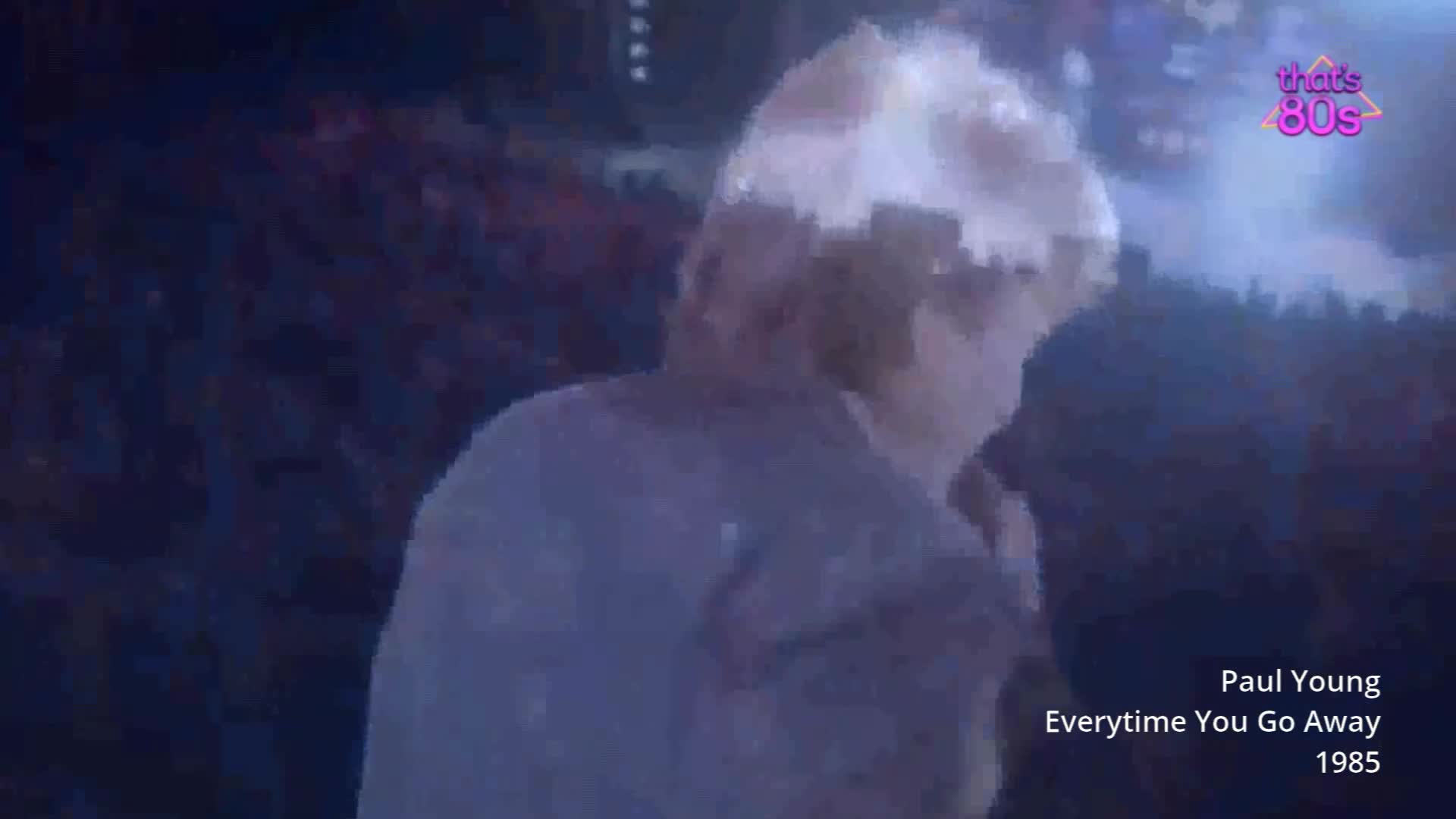 Paul Young is on stage, his blonde hair catching the light as he sings. The crowd behind him is a dark mass, a sea of faces illuminated by the stage lights.