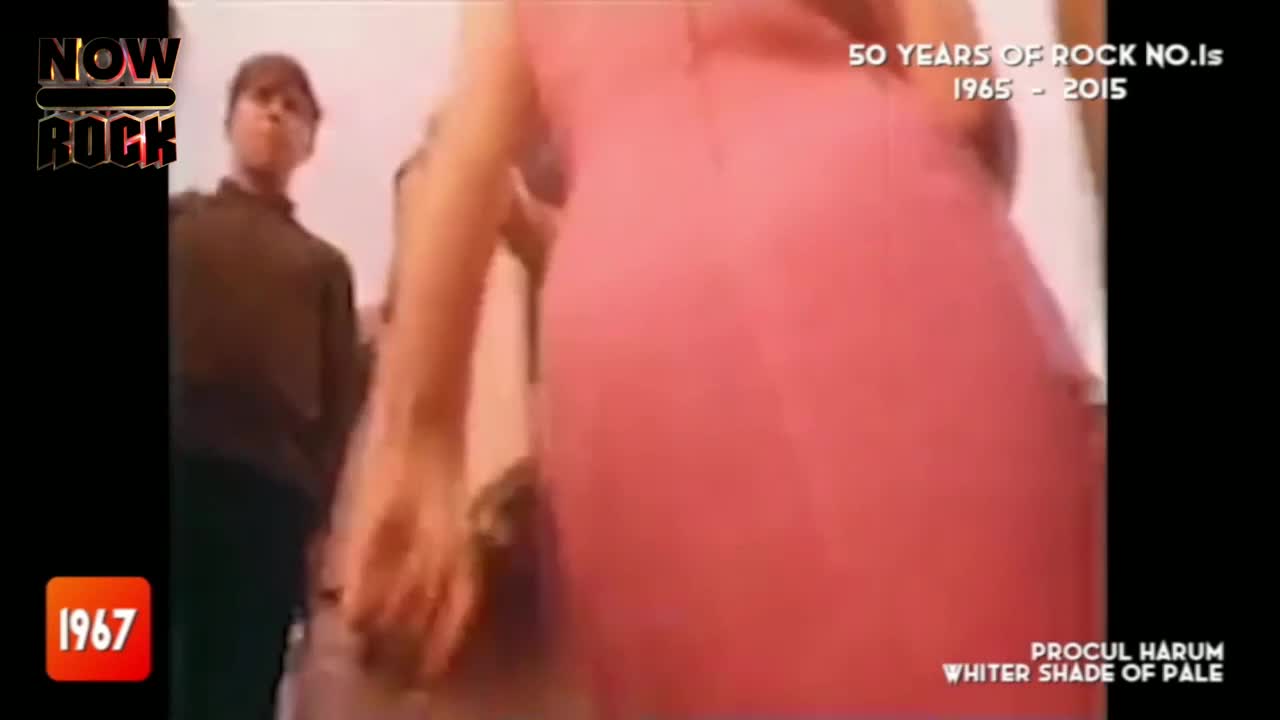 A woman in a pink dress is dancing, her back to the camera. A man in a dark sweater stands to the side, watching the performance.
