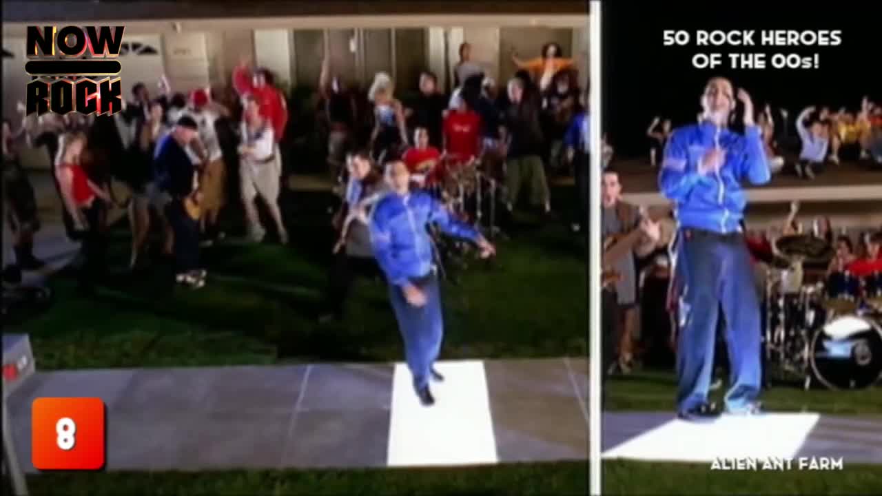 A band in blue jumpsuits dances on a lit-up square, while a crowd of people in casual clothes bops around on the lawn. The scene is part of a music video, as indicated by the "NOW Rock" logo.
