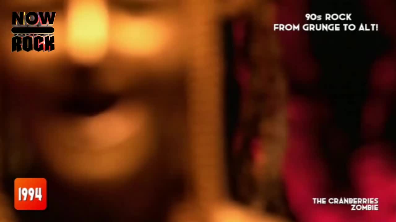 The image is bathed in warm, amber tones. A blurred face is visible, with the text "NOW ROCK" and "90s Rock" in the corner.
