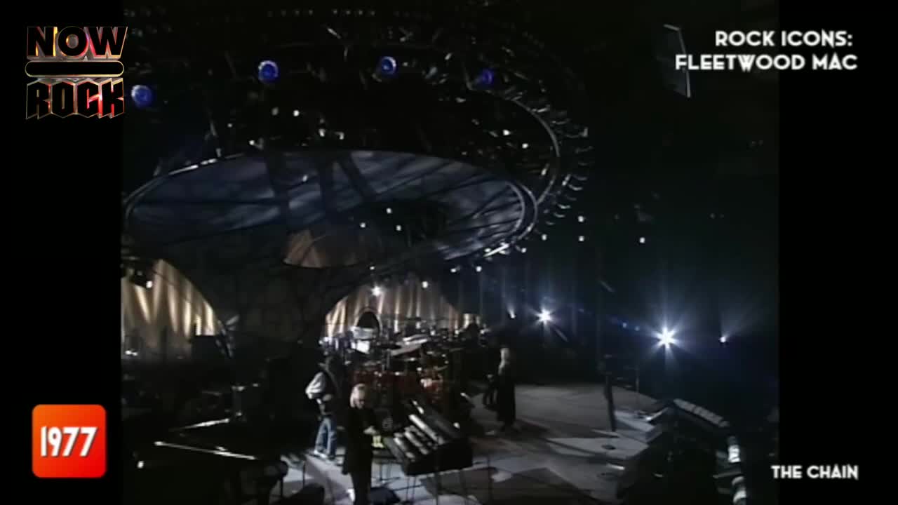 Under the stage lights, the band is silhouetted, a dark shape against the bright stage. The camera focuses on the musicians, who are ready to play "The Chain" on NOW Rock.

