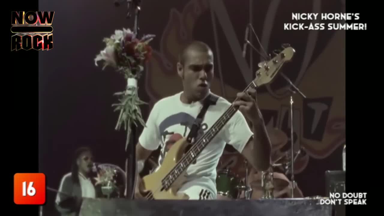 The bassist, wearing a white t-shirt, is focused on his instrument, fingers dancing across the fretboard. A bouquet of flowers sits to his left, a colorful contrast to the stage lights.
