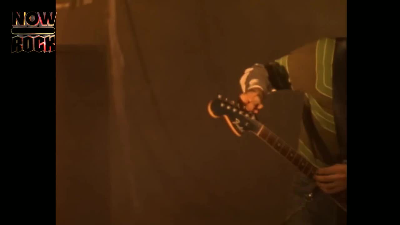 The guitarist is holding a Fender, the headstock angled towards the crowd. His fingers are poised, ready to strike the strings.

