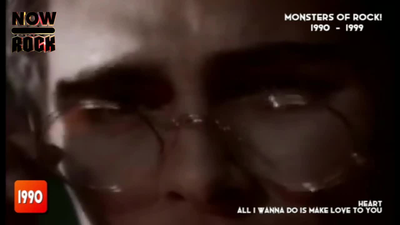 The face of a man wearing glasses fills the screen, his eyes reflecting light. The NOW Rock logo and "Monsters of Rock" are visible, along with the year 1990.
