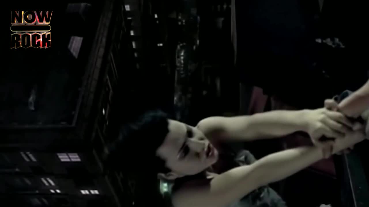 A woman is being held by the arms, her face contorted in what looks like panic. The scene is dark, with a cityscape barely visible in the background.
