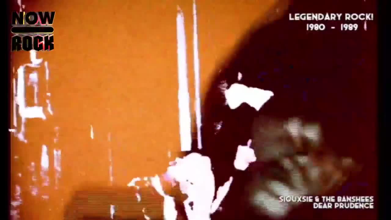 The screen is awash in orange, with a dark figure partially visible on the right. White streaks and shapes cut across the frame, and the NOW Rock logo is in the corner.
