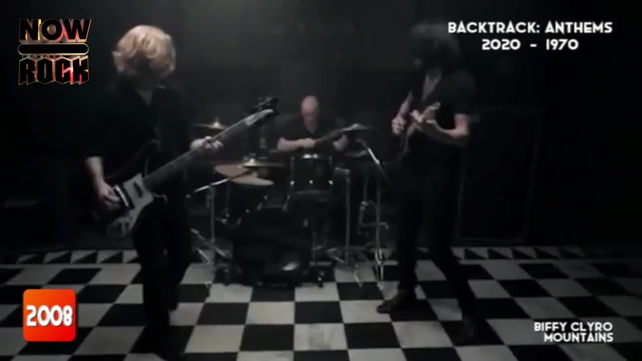 The band, Biffy Clyro, is playing a song, bathed in a dim light. The guitarist with the blonde hair is strumming his bass, while the drummer keeps the beat in the background.
