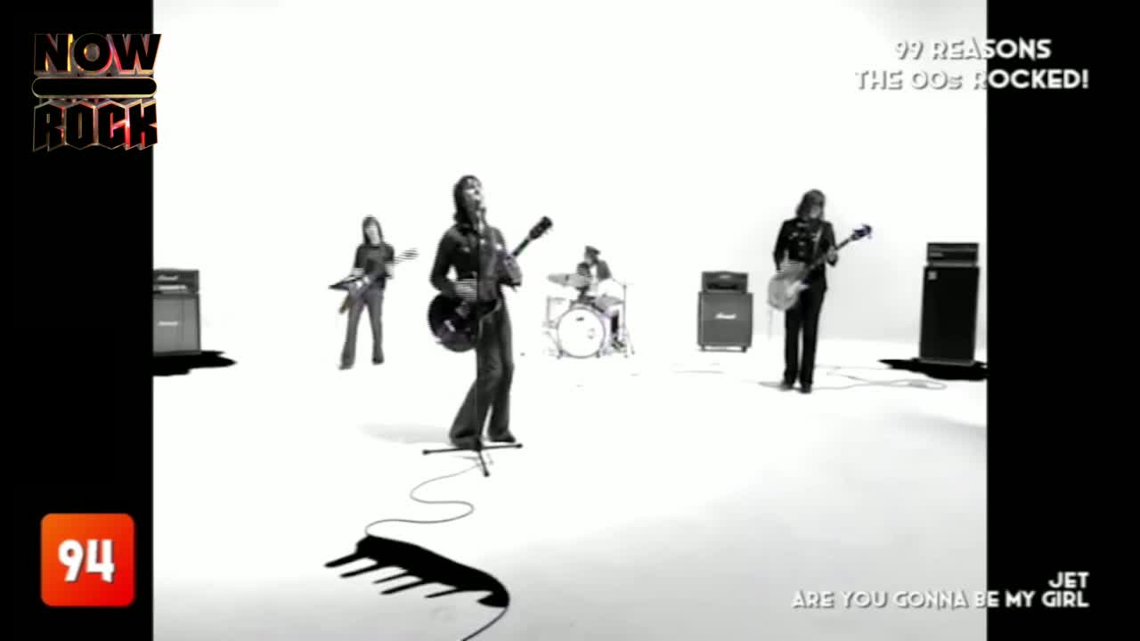The band, framed by a stark white backdrop, is playing "Are You Gonna Be My Girl" on NOW Rock. The lead singer, with his guitar, is front and center, while the drummer keeps the beat in the background.
