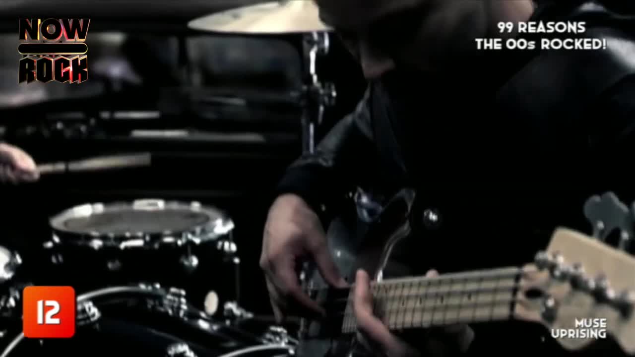 The guitarist's fingers dance across the fretboard, while the drummer's sticks strike the snare. It's a live performance, the energy palpable, with "Muse Uprising" on the screen.
