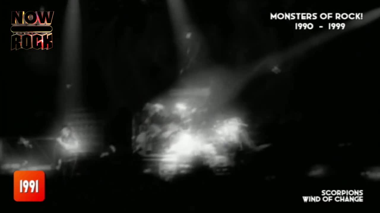 The stage is lit up, with the band members barely visible in the bright glare. A cloud of smoke hangs in the air, obscuring much of the action.
