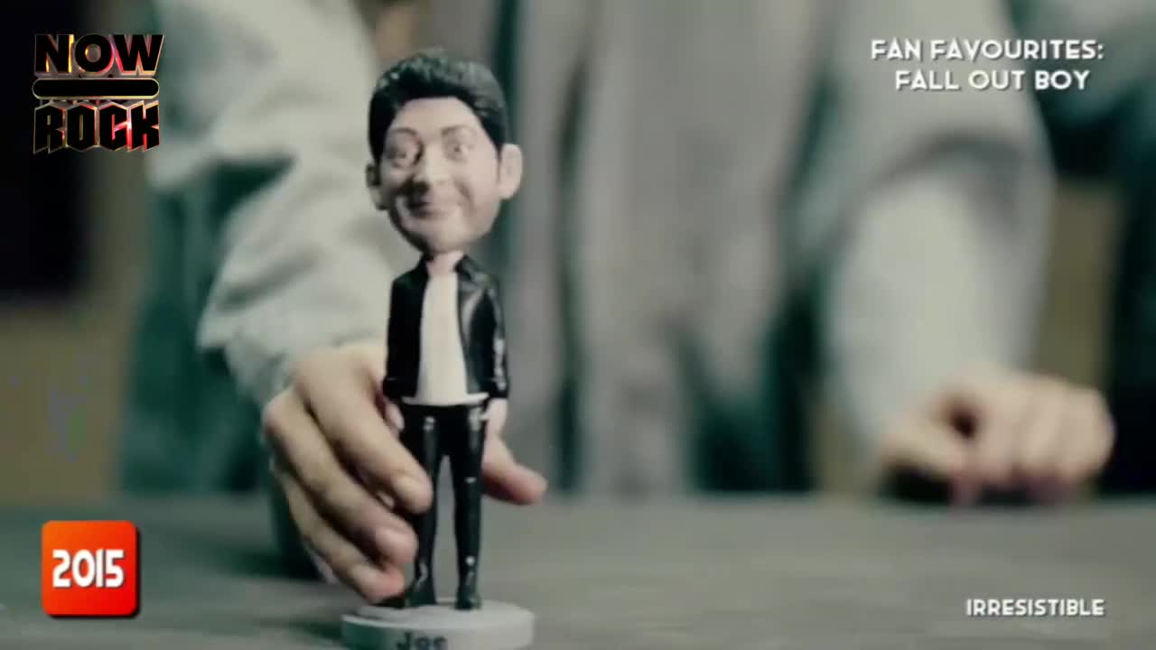 A bobblehead of a musician stands centered, held by a person's hands. The figure is stationary, but the hands around it suggest movement is imminent.
