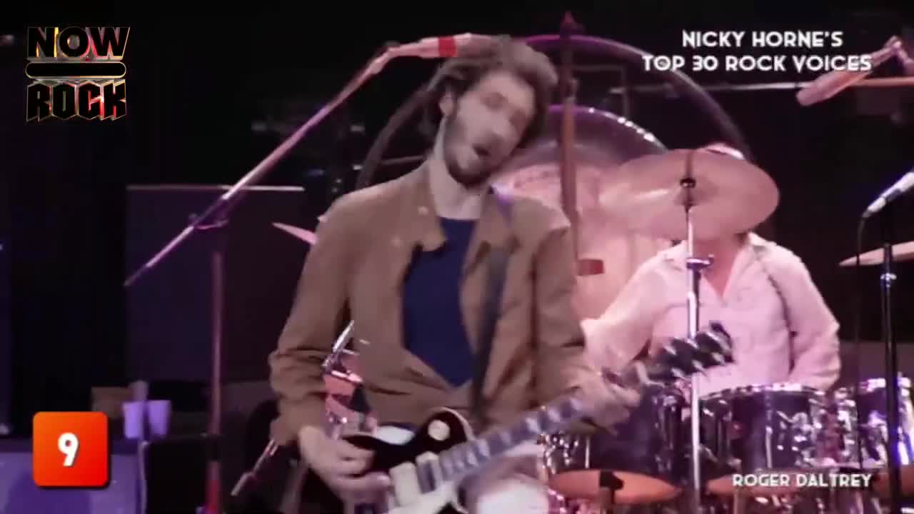 The guitarist, in a brown jacket, is singing with his head tilted back, his fingers moving over the fretboard of his black and white guitar. Behind him, the drummer is hitting the cymbals, the sound echoing through the venue.
