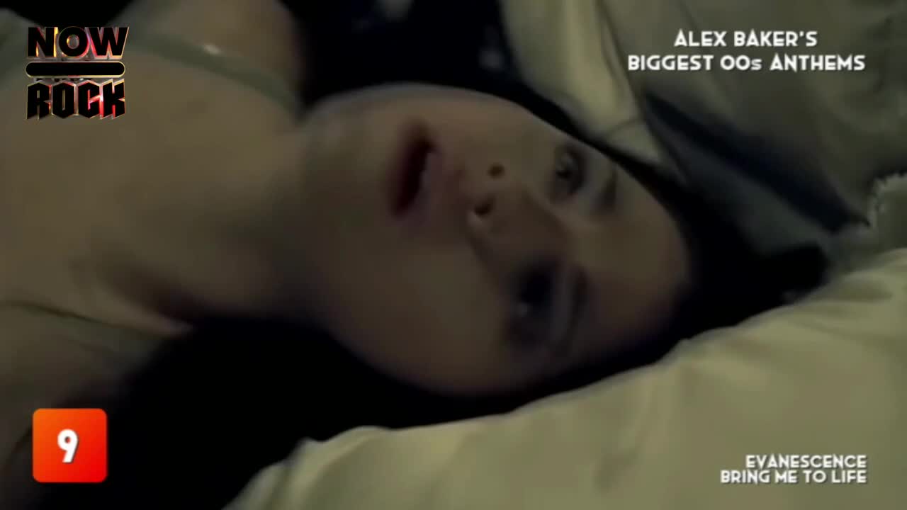 The woman lies on a bed, eyes open and looking upwards.  "Bring Me to Life" by Evanescence is playing on NOW Rock, with the song's title appearing on the screen.
