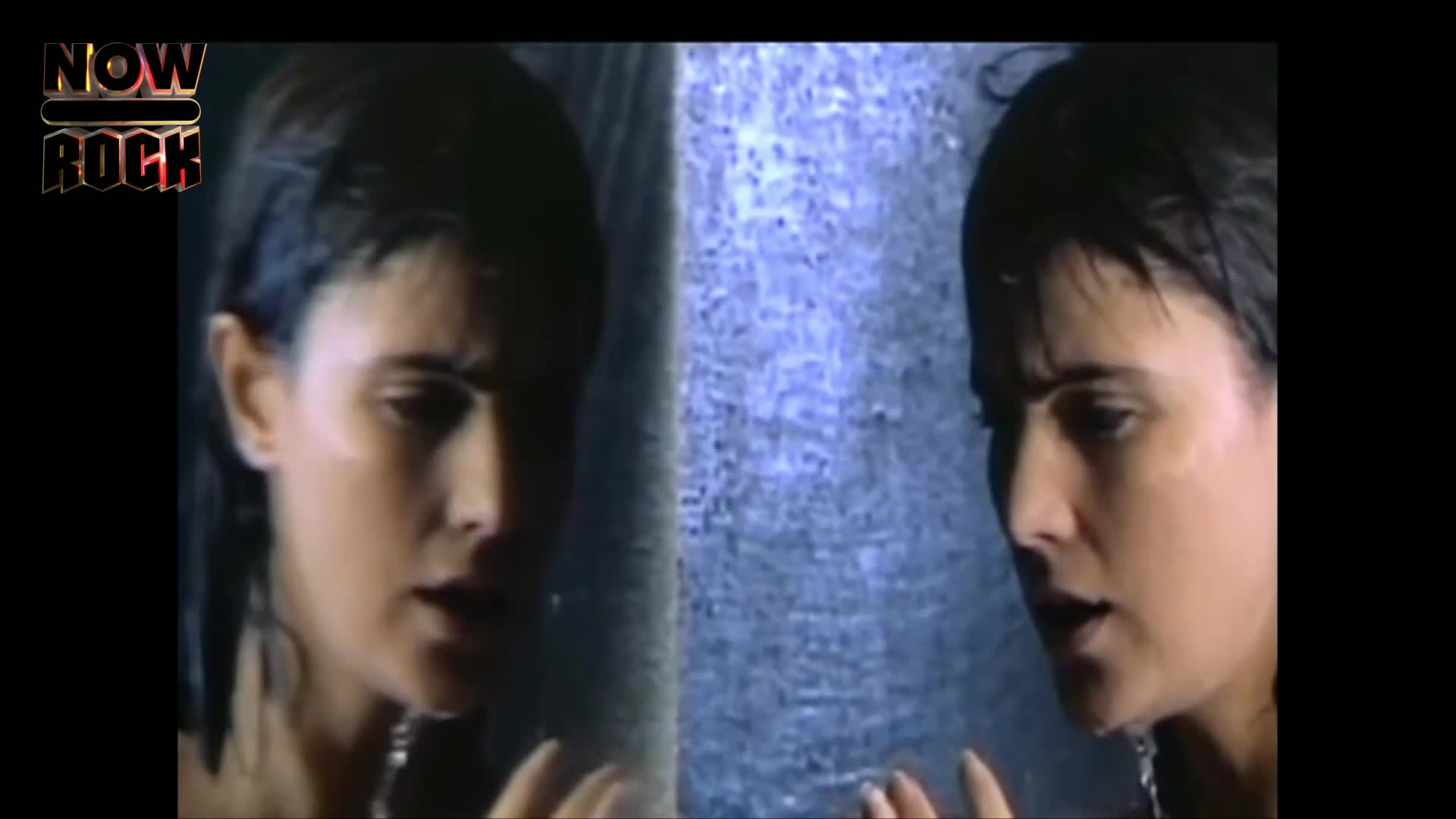 Water streams down the woman's face and hair, as she looks off to the side. Her reflection is right next to her, mirroring her expression.
