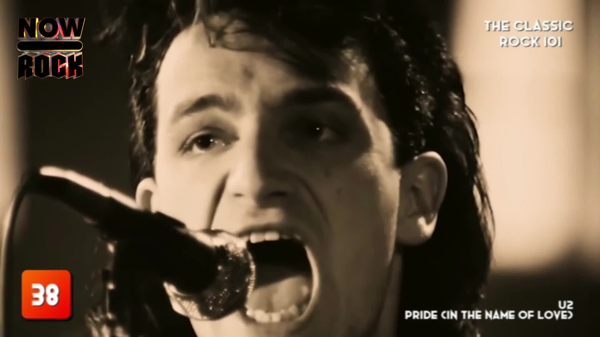 The singer's mouth is wide open, straining as he belts into the microphone. His dark hair is slicked back, and the intensity in his eyes is palpable.
