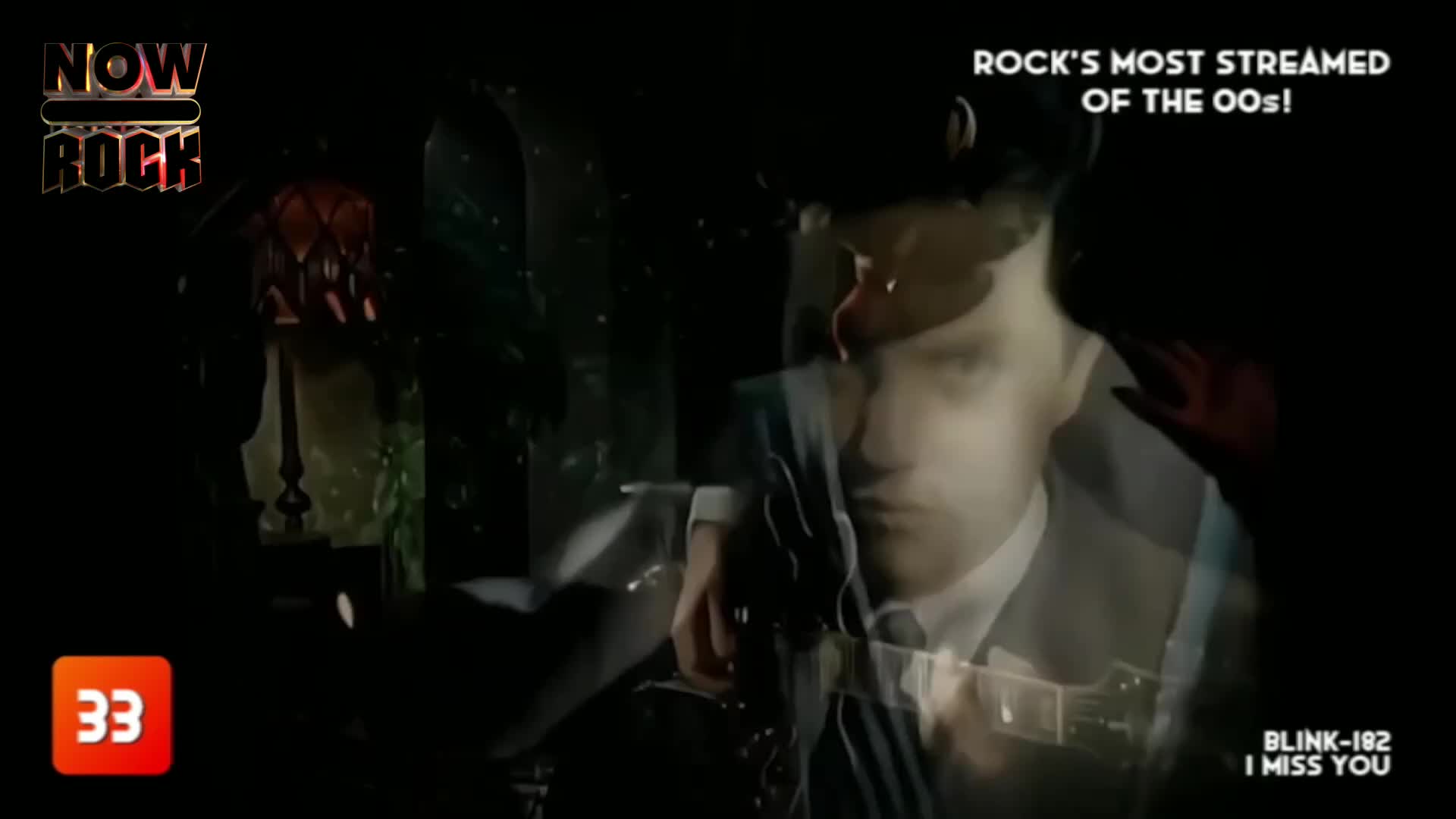 A young man in a suit, his face a pale overlay, strums a guitar. Beside him, a vintage lamp casts a dim glow on the dark, textured background.