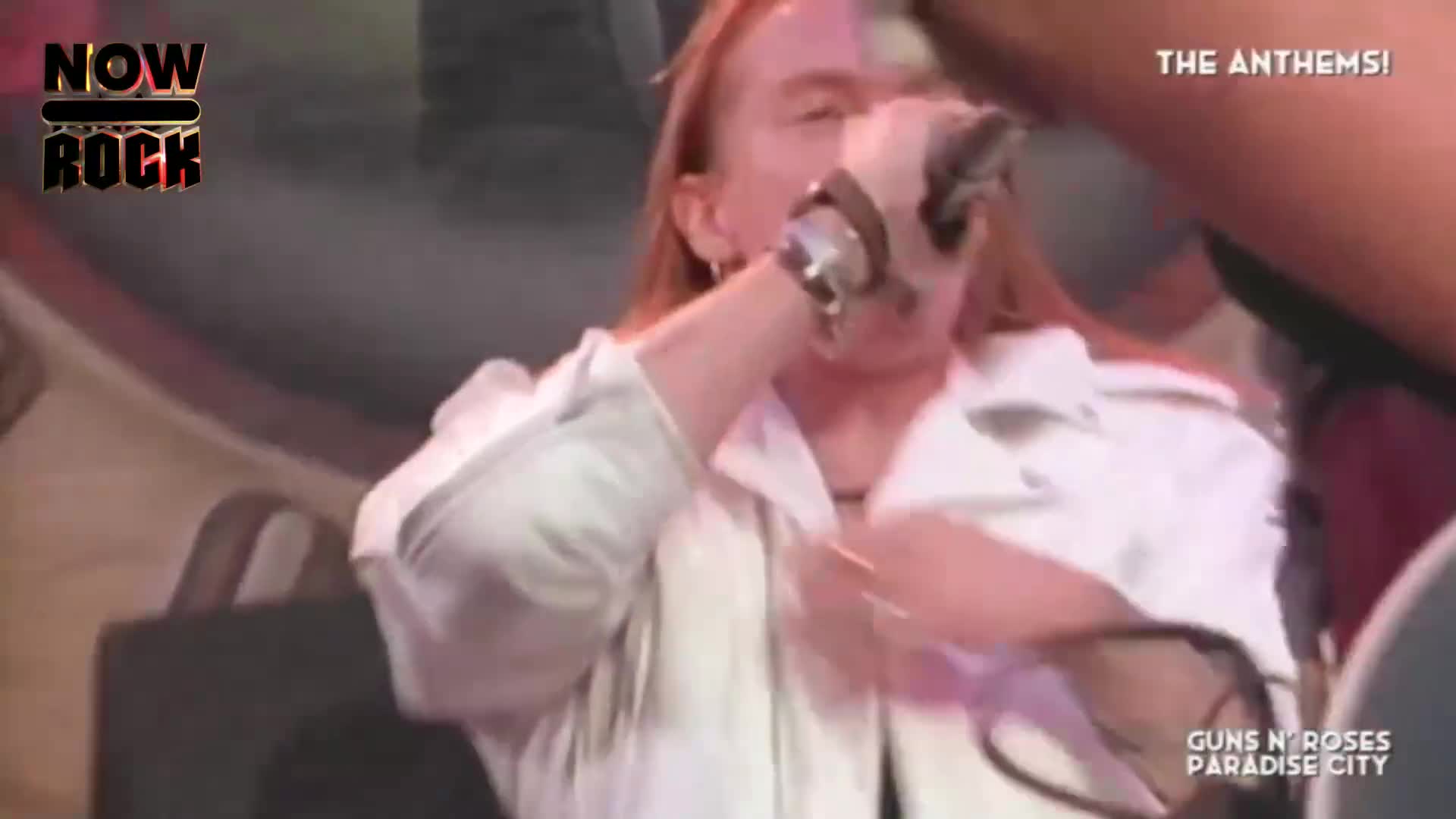The singer, with his long red hair, belts into the microphone, his white jacket catching the stage lights. The energy is palpable as he moves, a true rock performance unfolding.