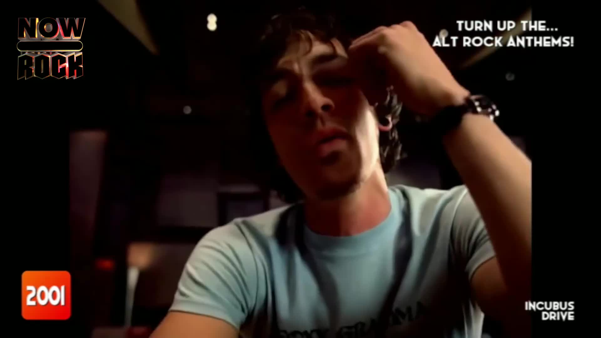 A young man with dark, curly hair runs his hand through his hair, his eyes closed. The "NOW Rock" logo and "TURN UP THE... ALT ROCK ANTHEMS!" text appear on screen.