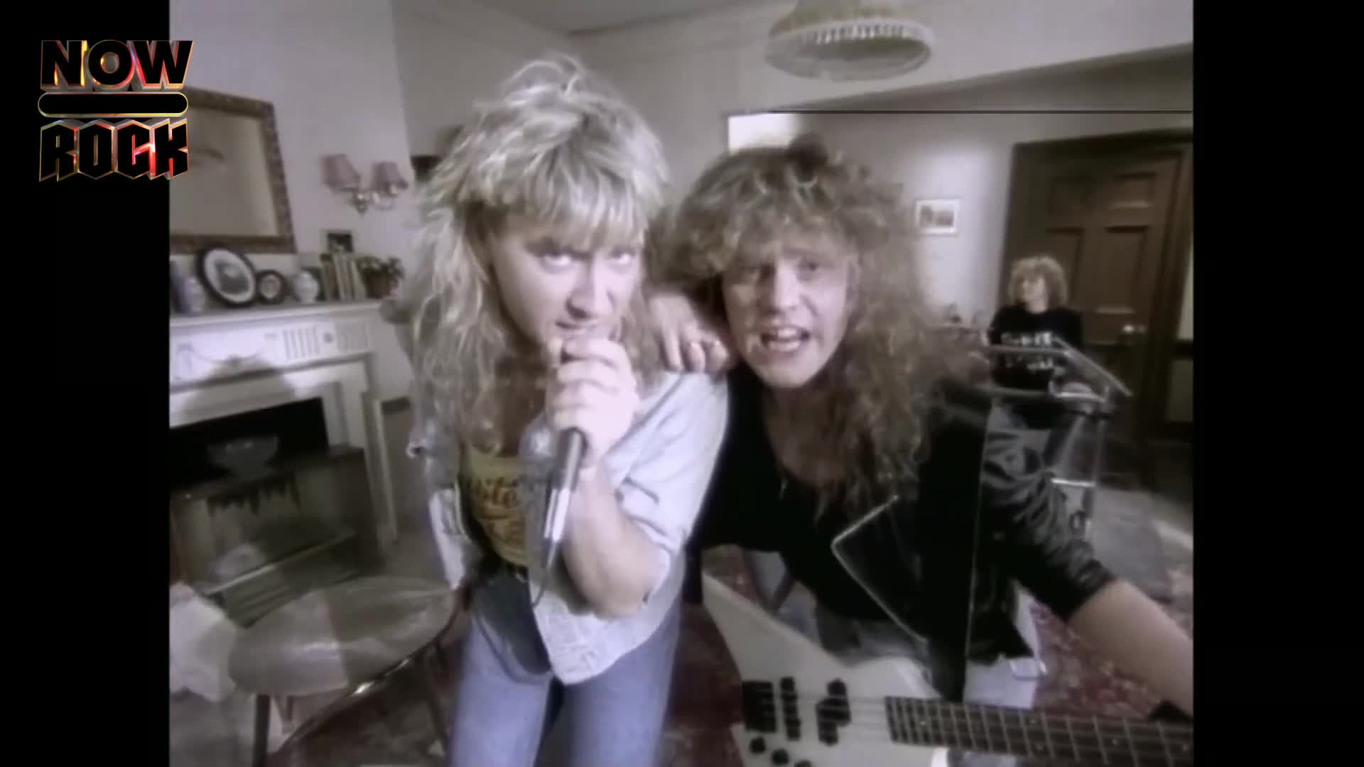 The singer leans into his microphone, his blonde hair falling across his face. Beside him, a guitarist grips his white bass, his own wild hair obscuring his expression.