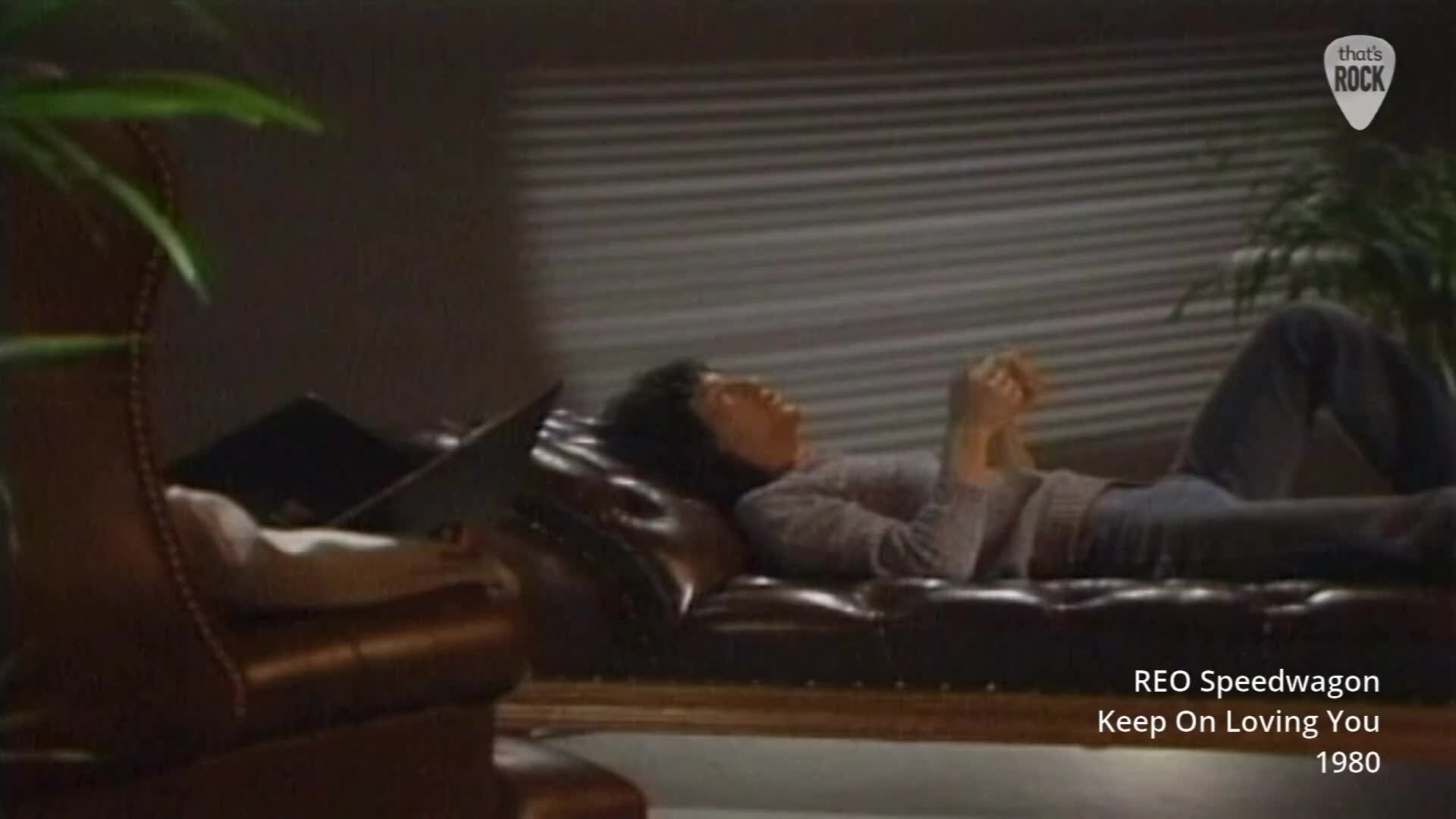 A man reclines on a dark leather couch, his head tilted back and hands clasped. The room is dimly lit, with blinds casting striped shadows across the wall behind him. A man reclines on a dark leather couch, his head tilted back and hands clasped. The room is dimly lit, with blinds casting striped shadows across the wall behind him.