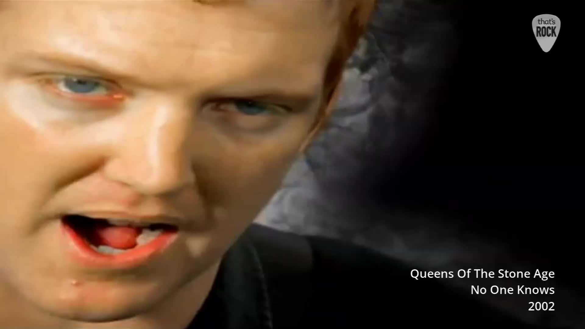 The singer's face fills the frame, his mouth open mid-song. A graphic overlay identifies Queens Of The Stone Age and their track "No One Knows" from 2002. The singer's face fills the frame, his mouth open mid-song. A graphic overlay identifies Queens Of The Stone Age and their track "No One Knows" from 2002.