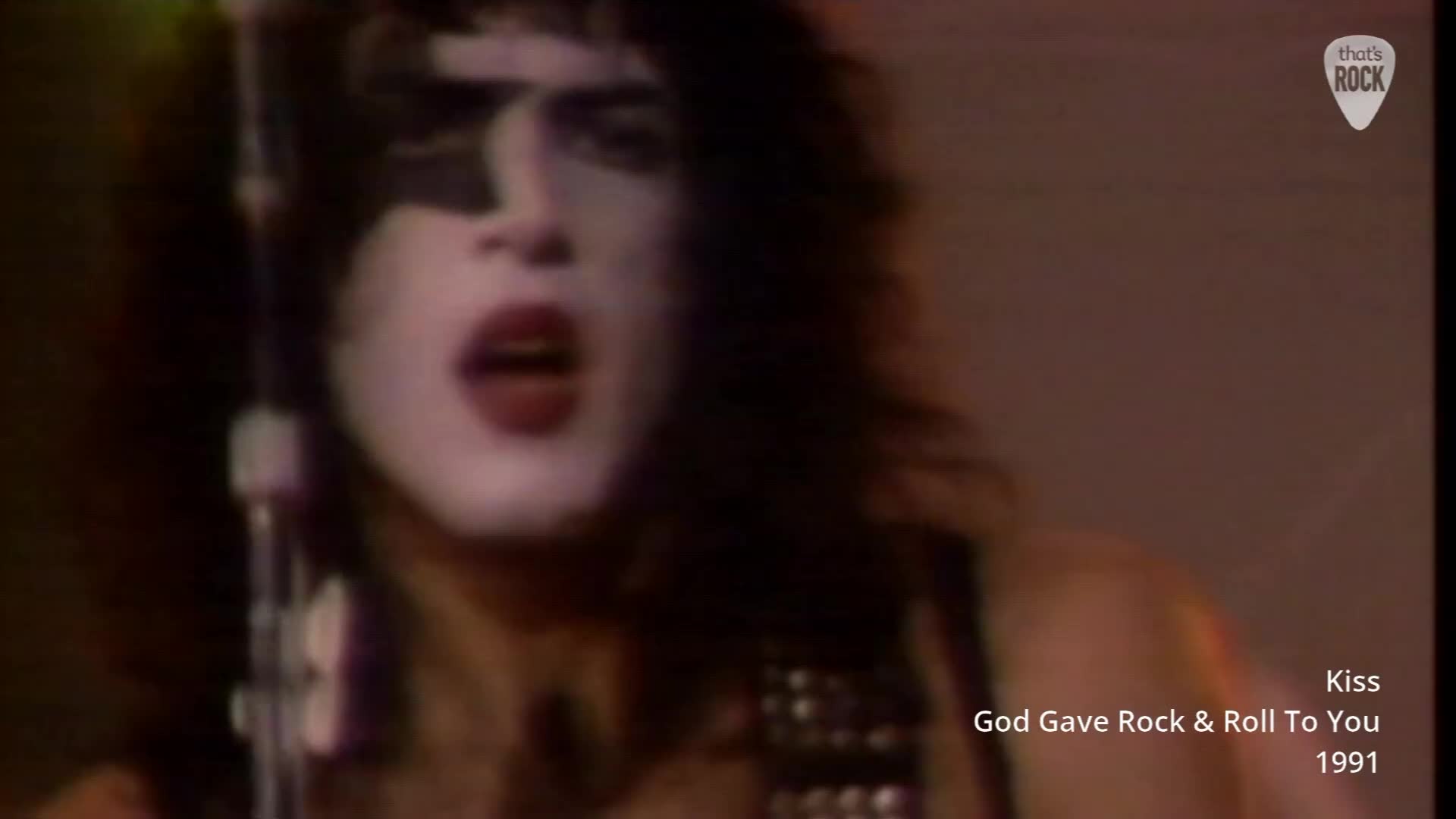 The singer's face, painted stark white with black accents, is tilted back as he belts out the lyrics. A microphone stand is positioned directly in front of his mouth, catching the raw energy of his performance. The singer's face, painted stark white with black accents, is tilted back as he belts out the lyrics. A microphone stand is positioned directly in front of his mouth, catching the raw energy of his performance.