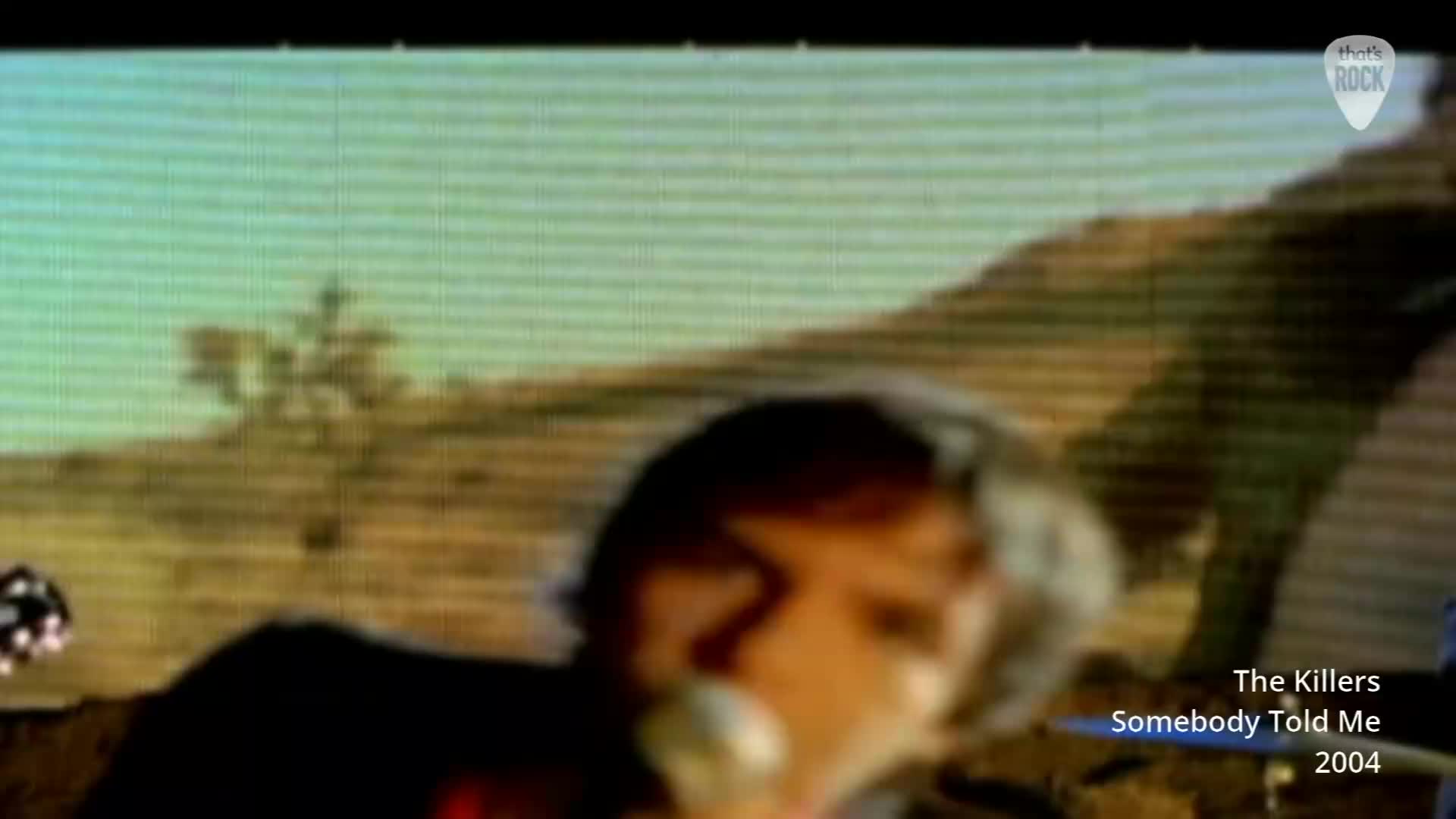 A man with light hair sings into a microphone, his face blurred with motion. Behind him, a desert landscape stretches out under a pale sky. A man with light hair sings into a microphone, his face blurred with motion. Behind him, a desert landscape stretches out under a pale sky.