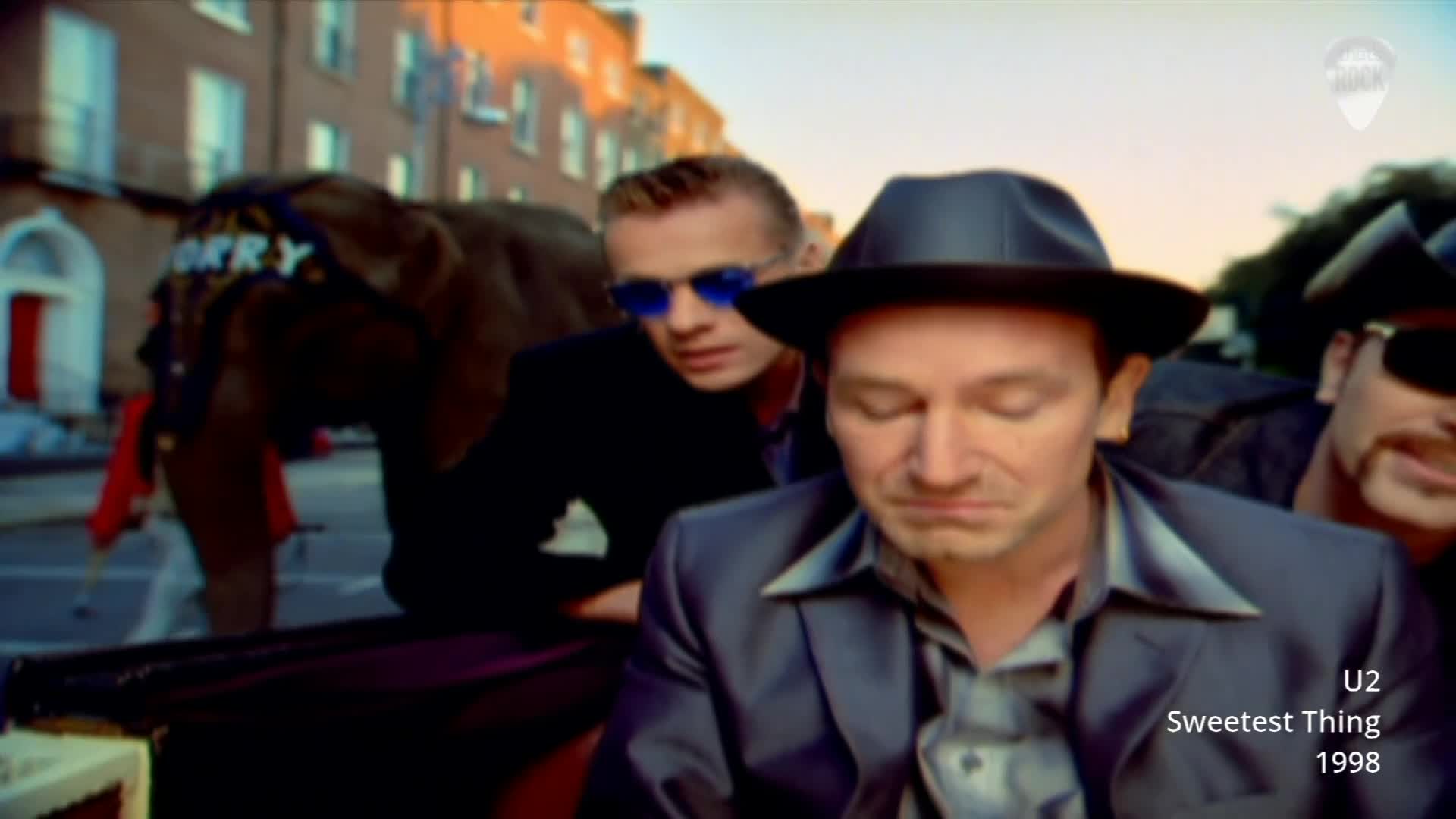 An elephant, adorned with "ERRY" on its headgear, ambles down a street in Dublin. Bono, wearing a fedora, sits in the foreground, eyes closed, as the band's music fills the air. An elephant, adorned with "ERRY" on its headgear, ambles down a street in Dublin. Bono, wearing a fedora, sits in the foreground, eyes closed, as the band's music fills the air.