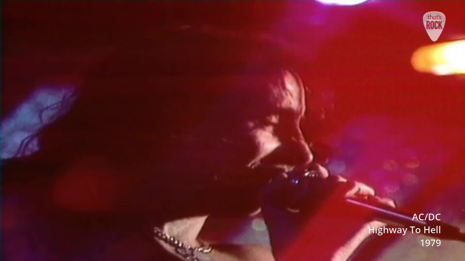 The singer's face is illuminated by a harsh red light as he belts into the microphone. His long dark hair whips around his head, a testament to the energy of the performance. The singer's face is illuminated by a harsh red light as he belts into the microphone. His long dark hair whips around his head, a testament to the energy of the performance.