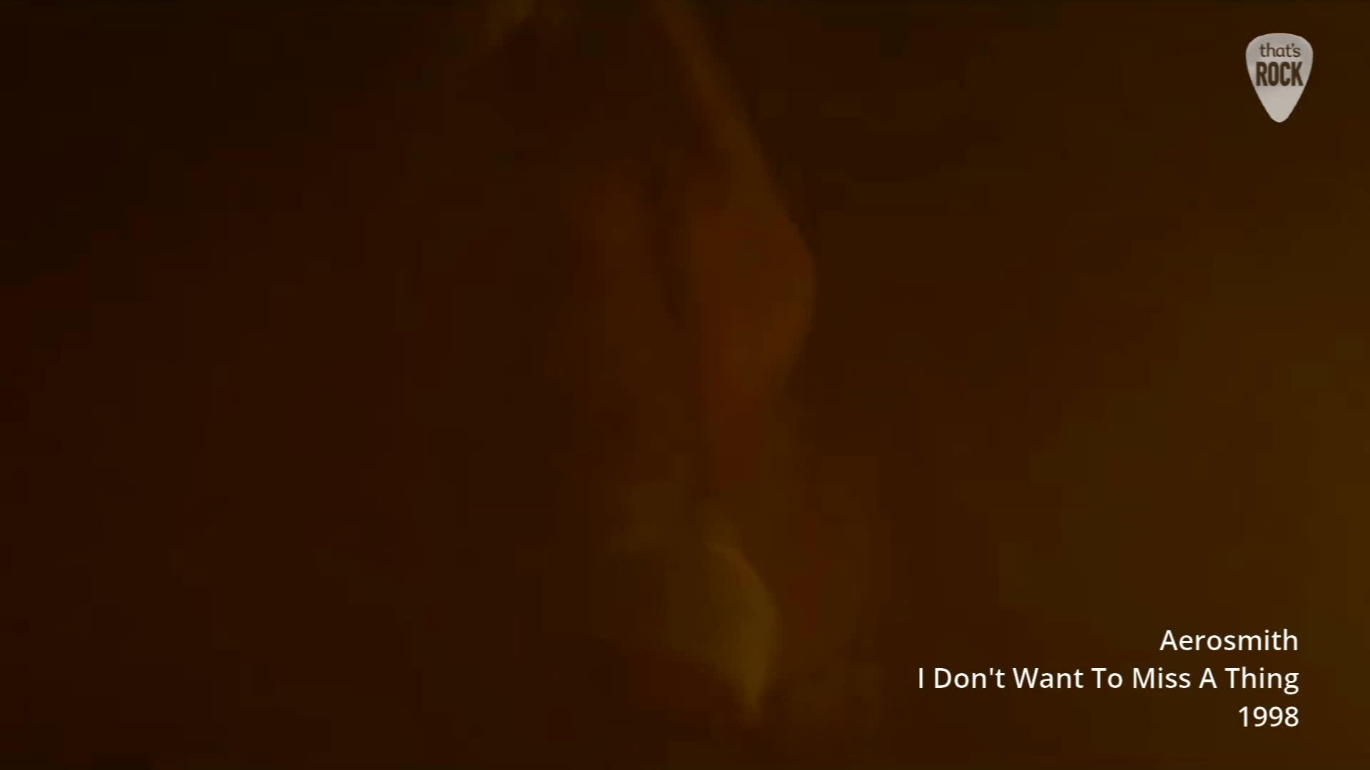 A figure moves through hazy, amber light, their form indistinct. The text below identifies this as Aerosmith's "I Don't Want To Miss A Thing" from 1998. A figure moves through hazy, amber light, their form indistinct. The text below identifies this as Aerosmith's "I Don't Want To Miss A Thing" from 1998.