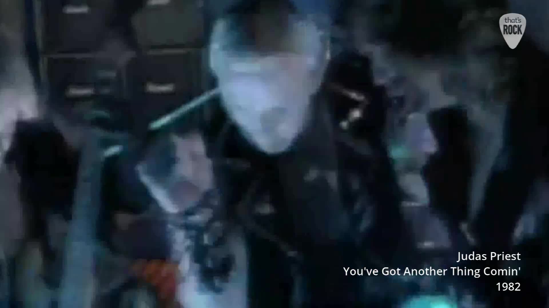 A man in a black leather jacket, his face pale and lit by blue light, sings intensely into a microphone. The stage behind him is dark, with hints of flashing lights.