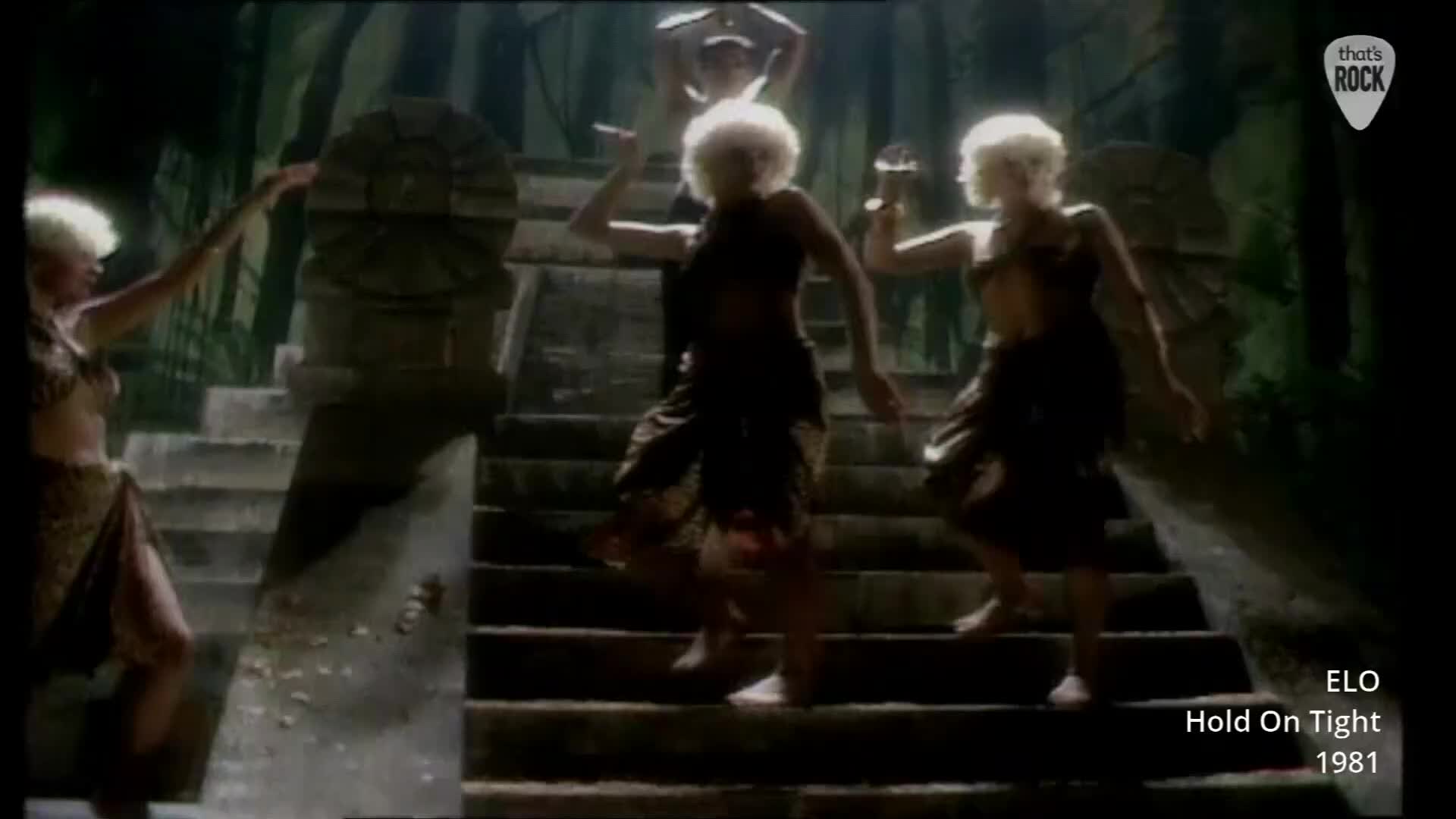 A group of women with bright blonde hair dance on stone steps, their movements energetic. The scene feels like a forgotten ritual, lit by an unseen, dramatic light source.