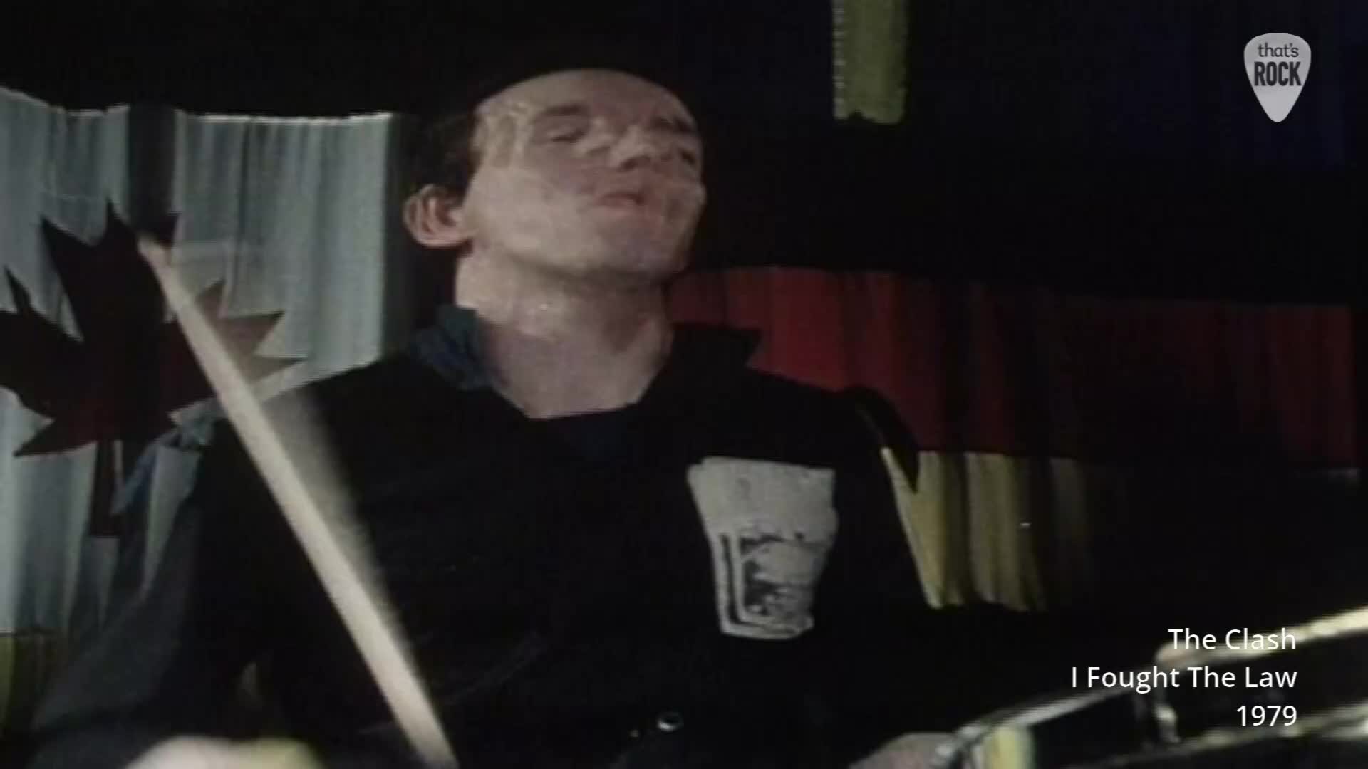 The drummer's sweat glistens under the lights as he pounds out the rhythm. Behind him, a Canadian maple leaf flag hangs against a dark backdrop.