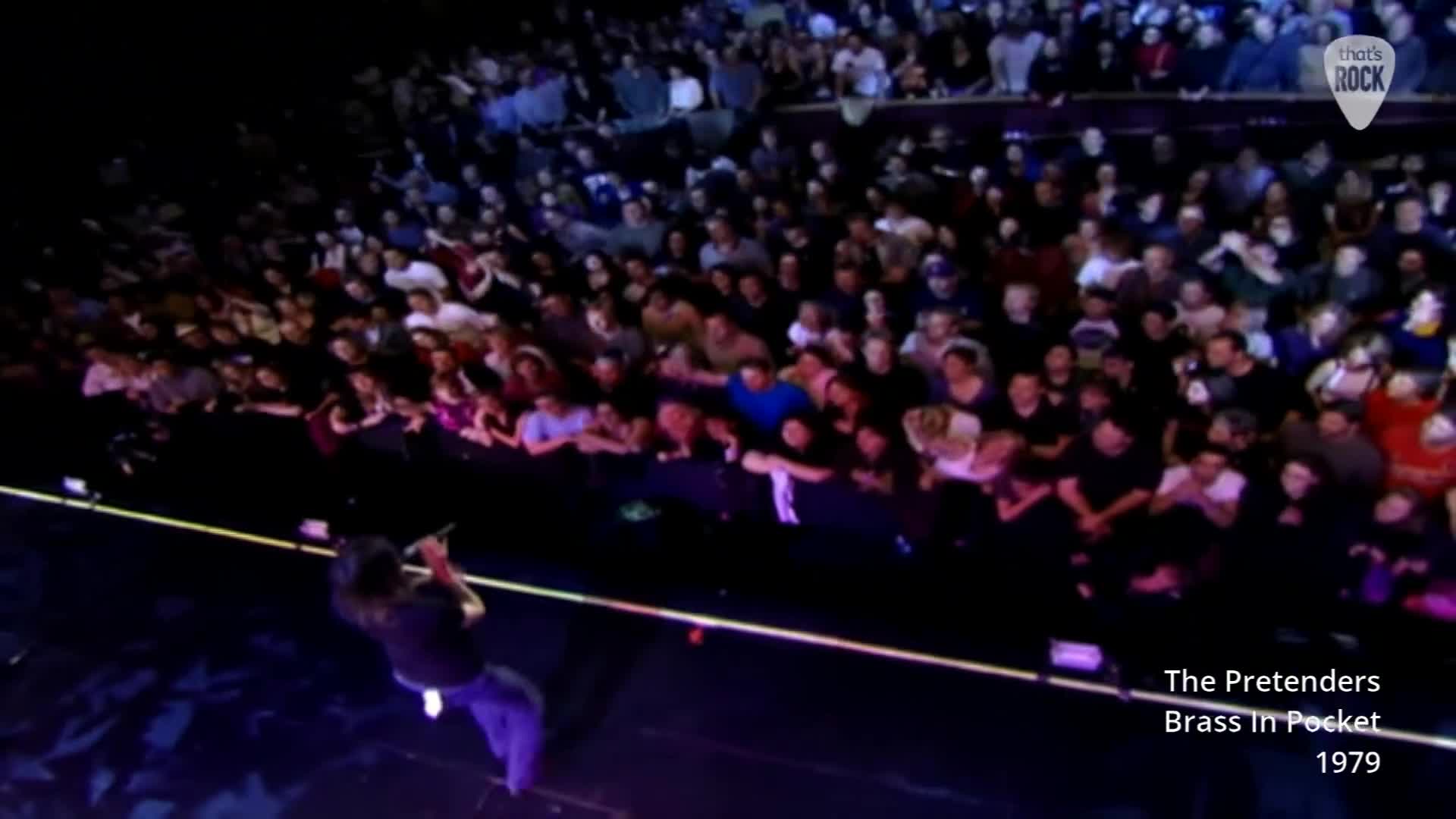 Chrissie Hynde belts out "Brass in Pocket" while a packed crowd in the UK watches intently. The energy is palpable as she commands the stage.