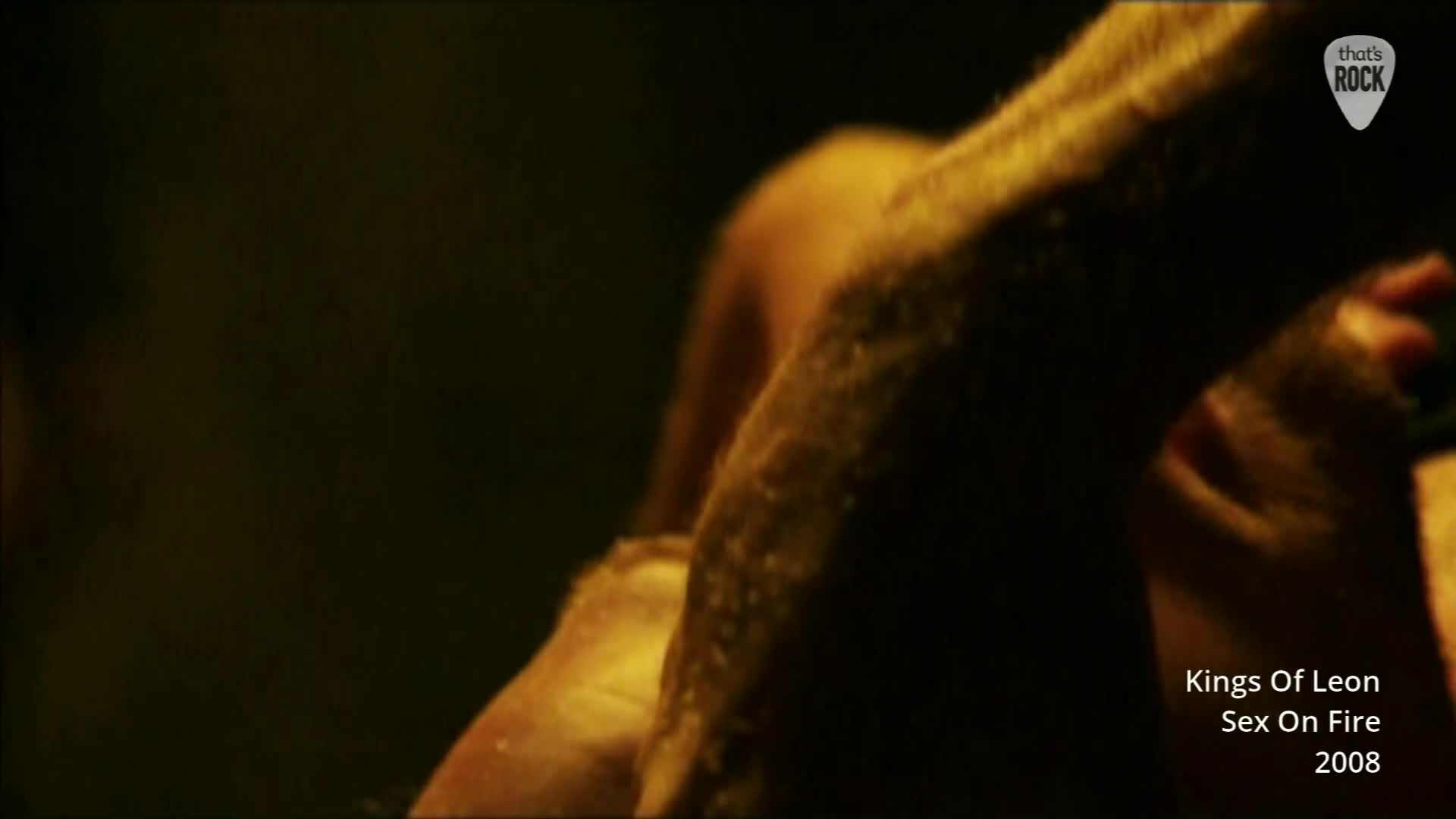 A man's arm, slick with sweat, moves against a dark background. The camera captures a close-up of this intense moment, likely from a live performance.