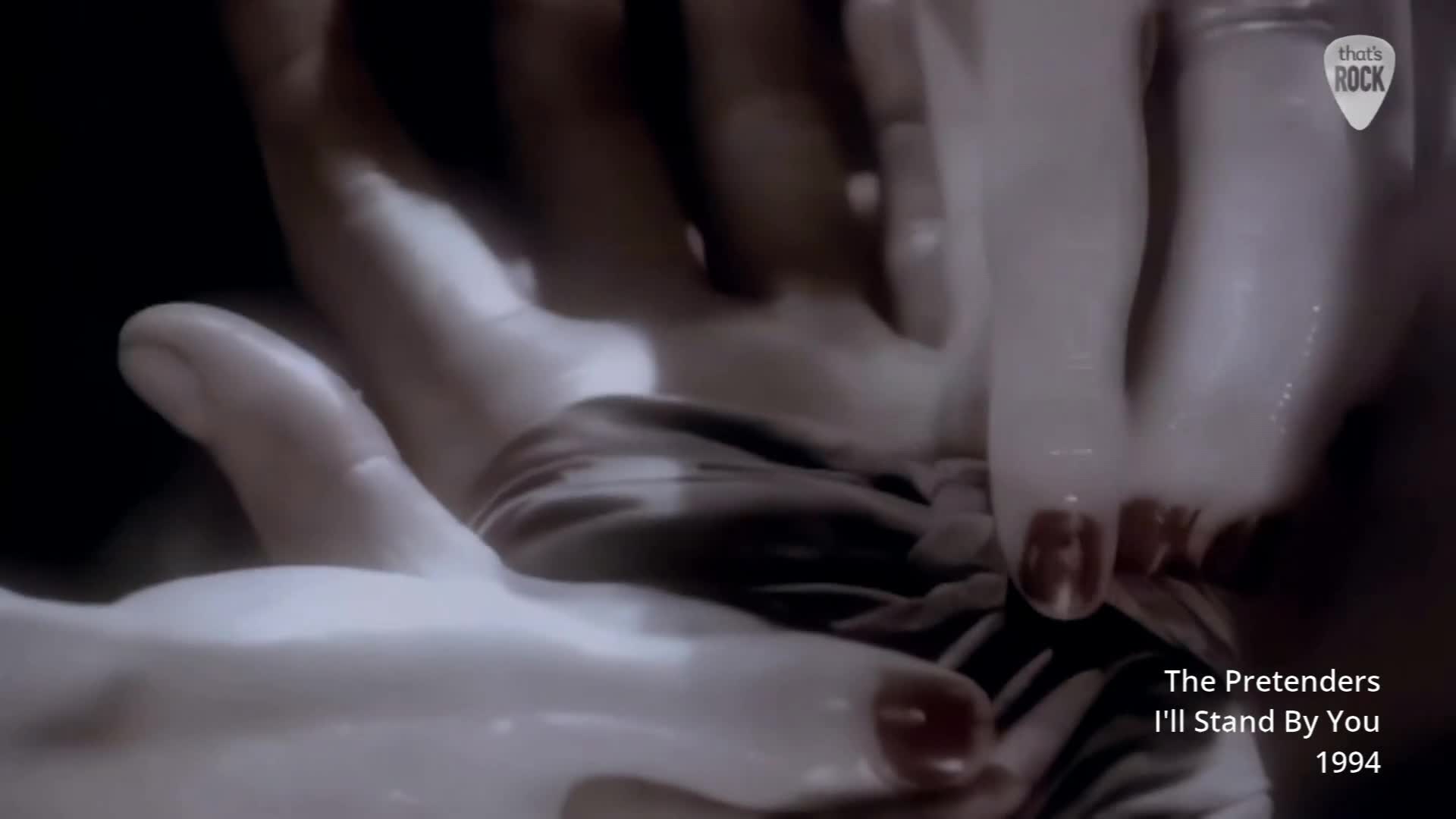 A bare foot, painted with dark red polish, presses down onto a dark, textured fabric. Hands, slick with something, cradle the foot from below.