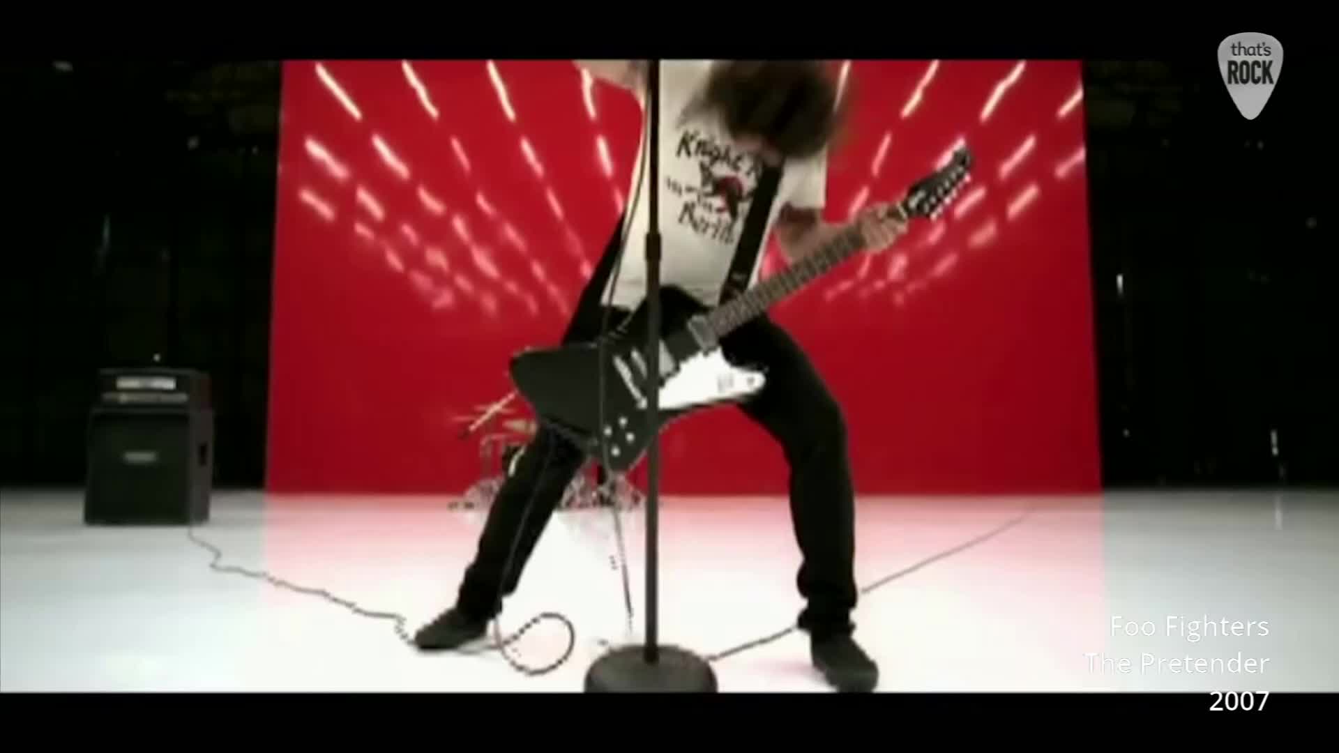 A guitarist thrashs his black Gibson Explorer, head whipping back and forth. His white t-shirt, emblazoned with what looks like a band logo, strains against his movements.