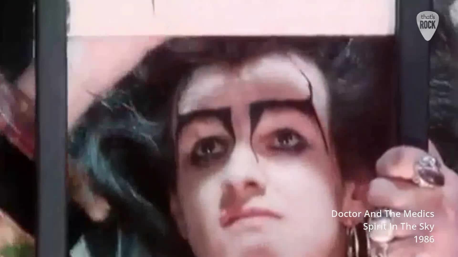 A person with striking black makeup and dark hair is looking directly at me. Their gaze is intense, framed by bold, angular eyebrows.