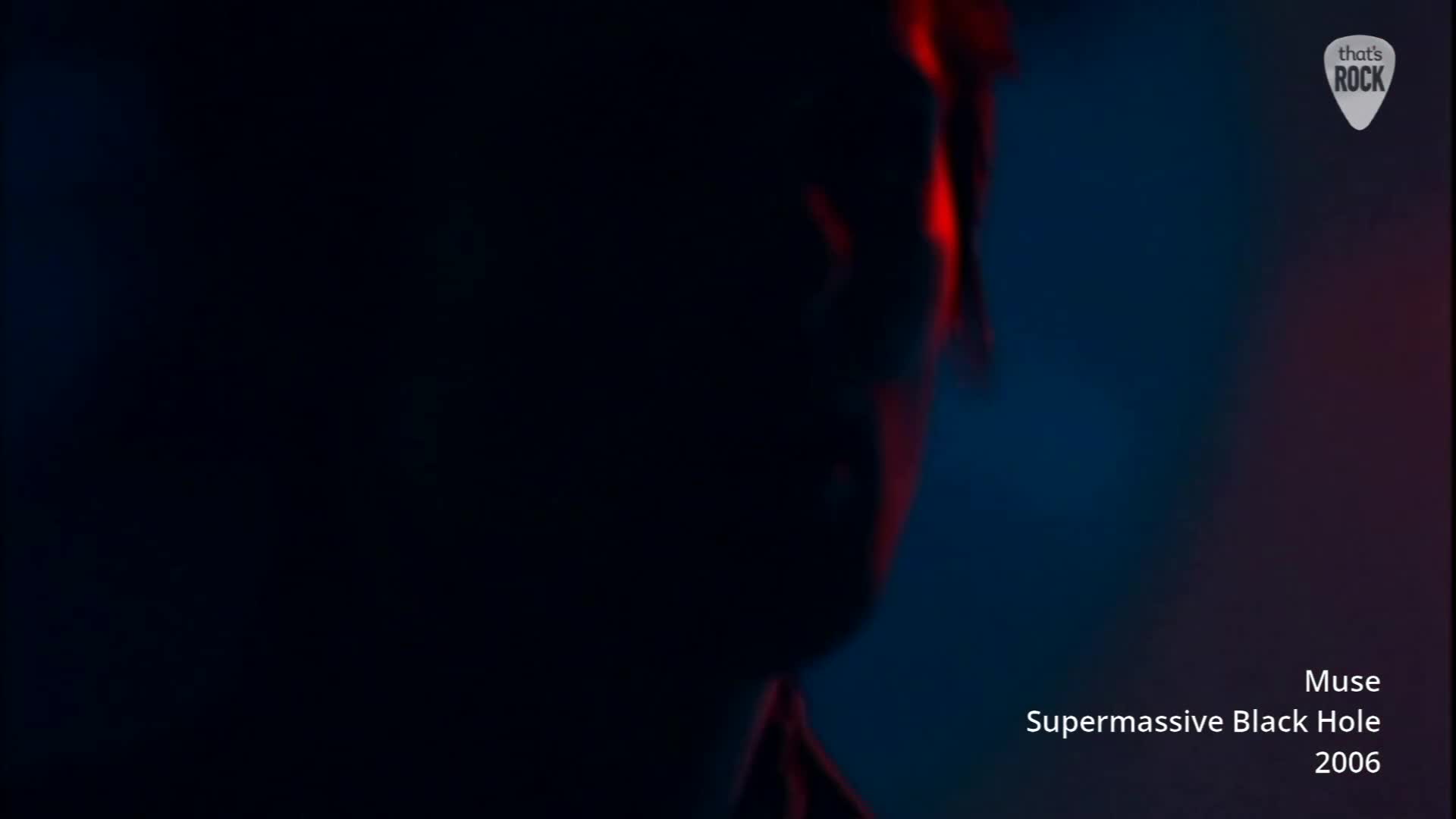 A figure's face is barely visible, illuminated by a stark red light against a dark blue background. Text at the bottom identifies this as Muse's "Supermassive Black Hole" from 2006.