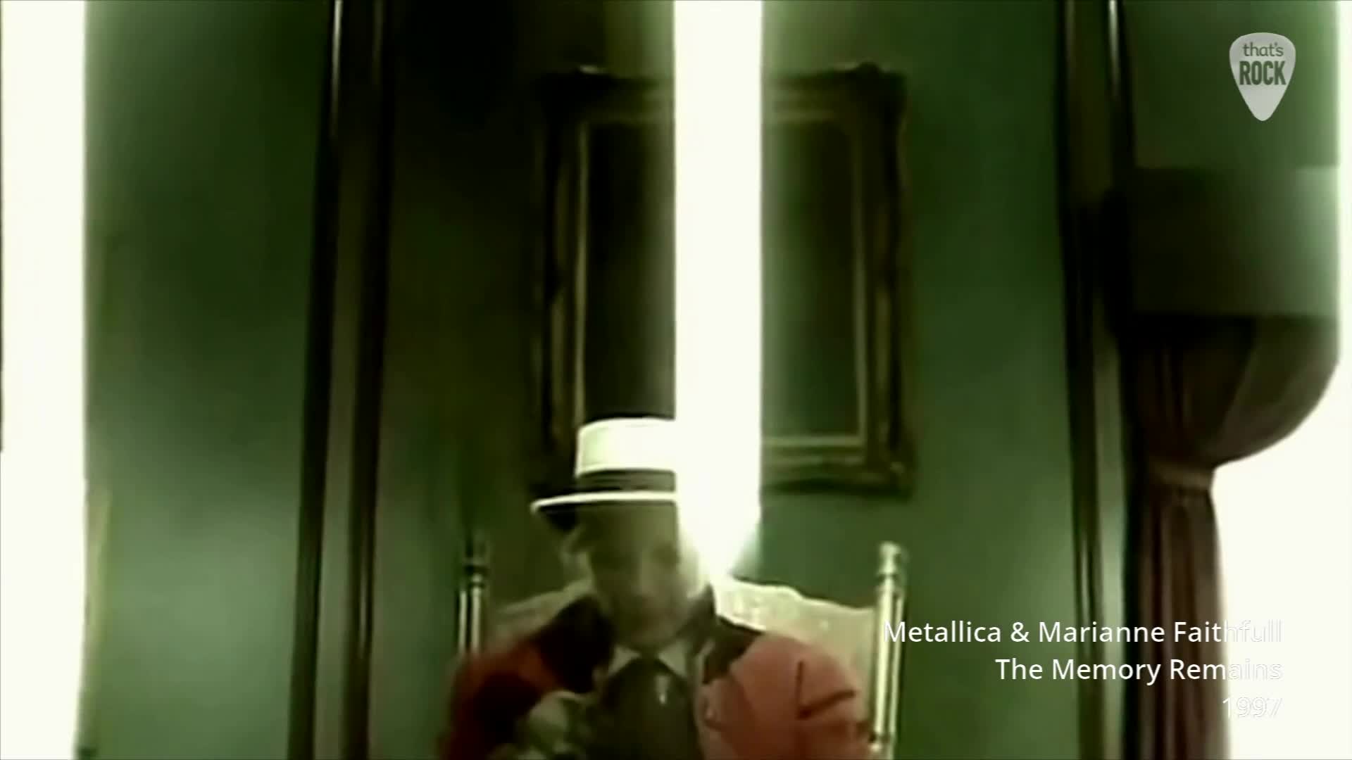 A man in a white hat and red jacket sits in a chair, bathed in a bright, vertical shaft of light. The walls around him are a deep, muted green.