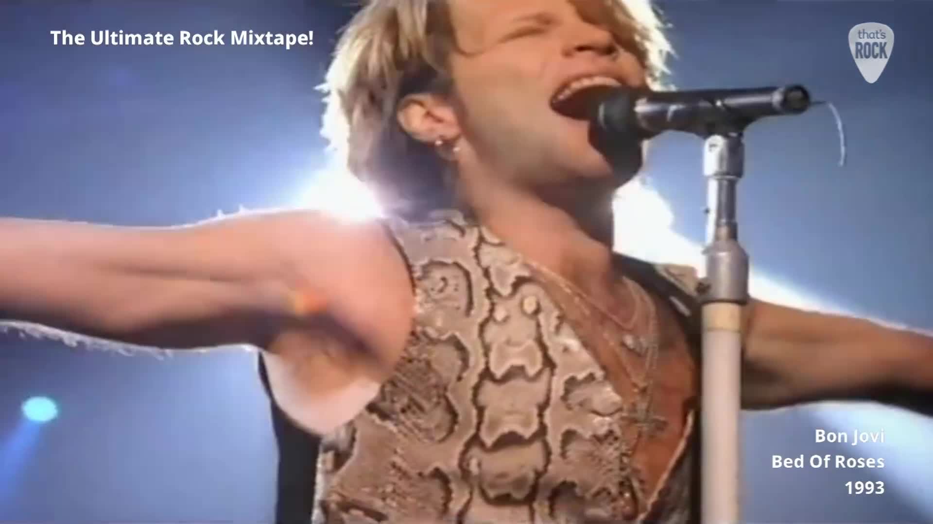 The singer's arms are outstretched as he belts into the microphone. His snakeskin vest catches the bright stage lights.