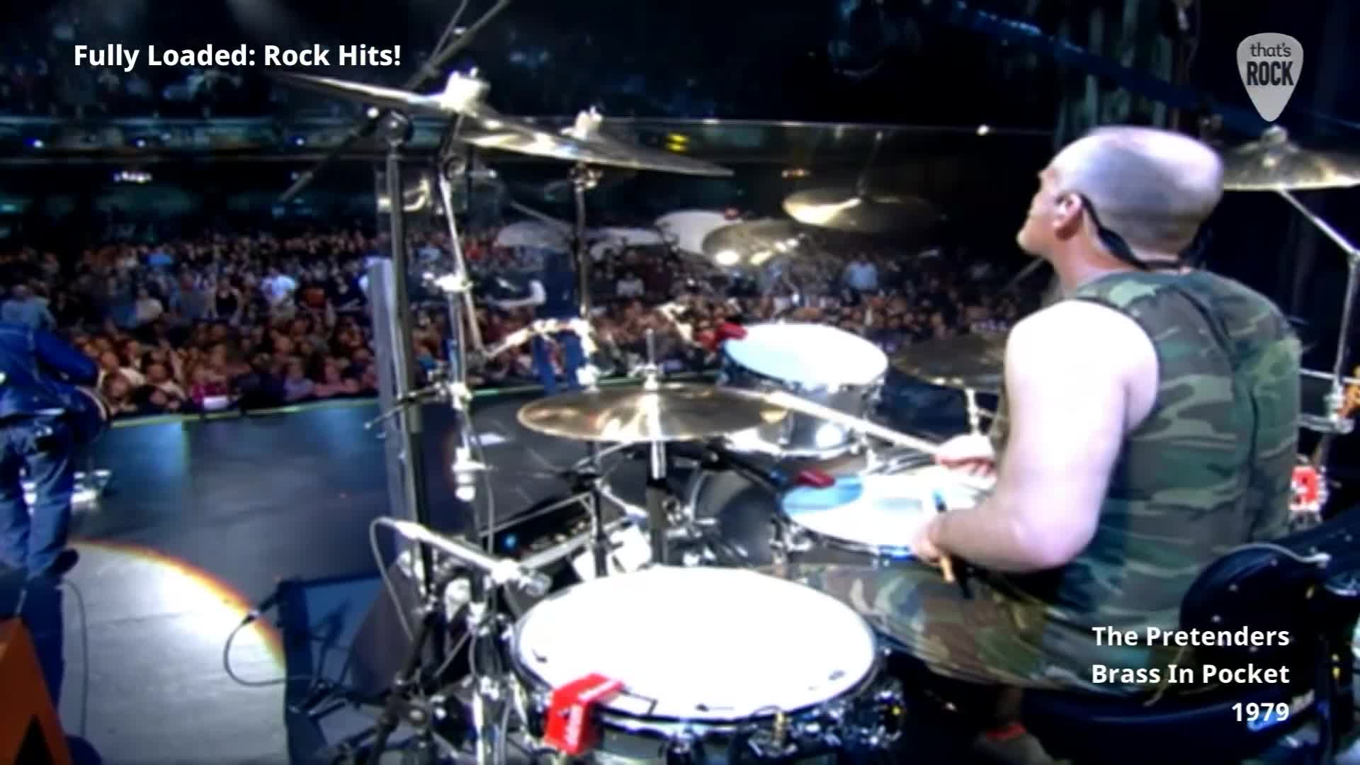 The drummer's sticks are a blur as they hit the snare drum, a powerful beat echoing through the packed arena. A massive crowd stretches out before the stage, a sea of faces illuminated by the stage lights.