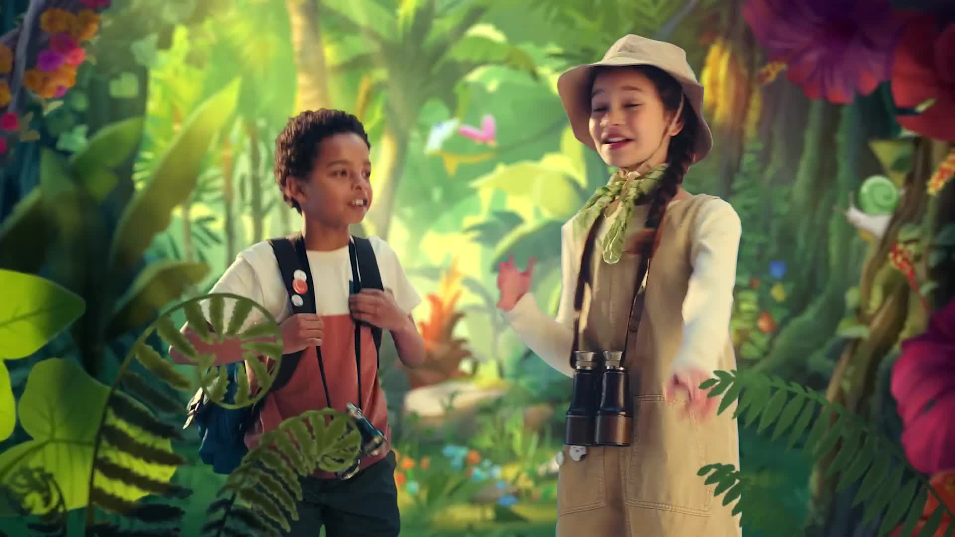 Two children, dressed in explorer outfits, stand in front of a lush, cartoon jungle backdrop. The girl gestures with her hands, while the boy looks on, both seemingly mid-conversation.
