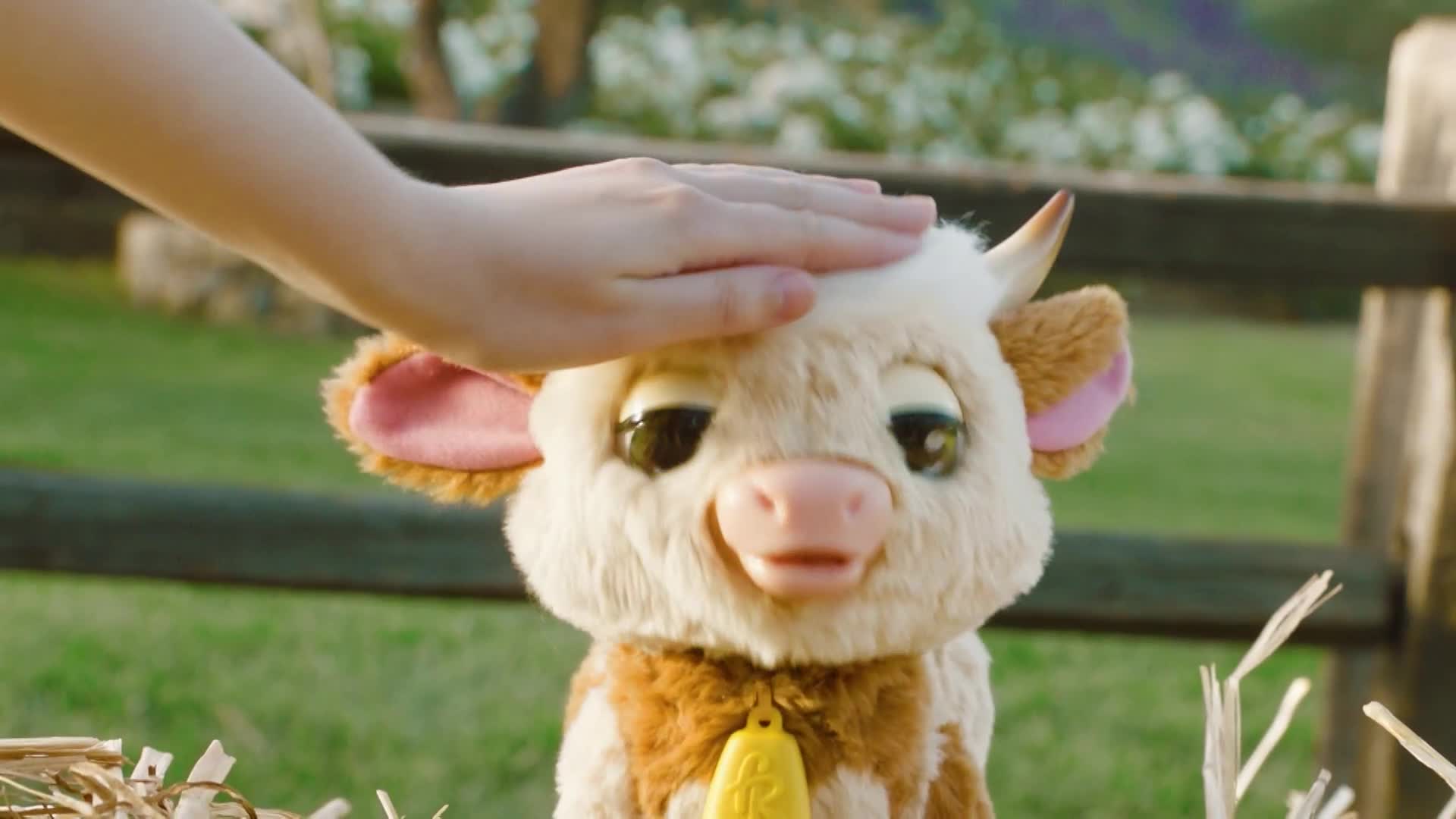 A hand gently strokes the soft, plush head of a toy cow. Its big, dark eyes seem to close slightly as it's petted.
