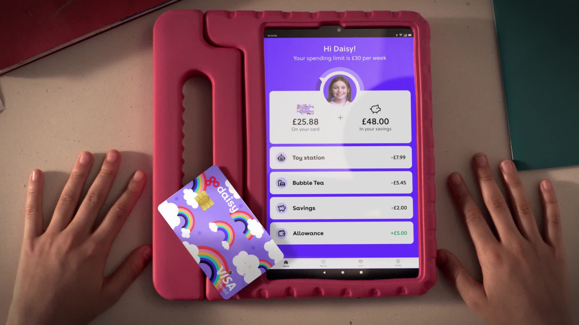 A tablet displays a financial app with a girl's photo, showing spending and savings amounts. Next to it rests a colorful Visa card with rainbows and the "go daisy" logo.

