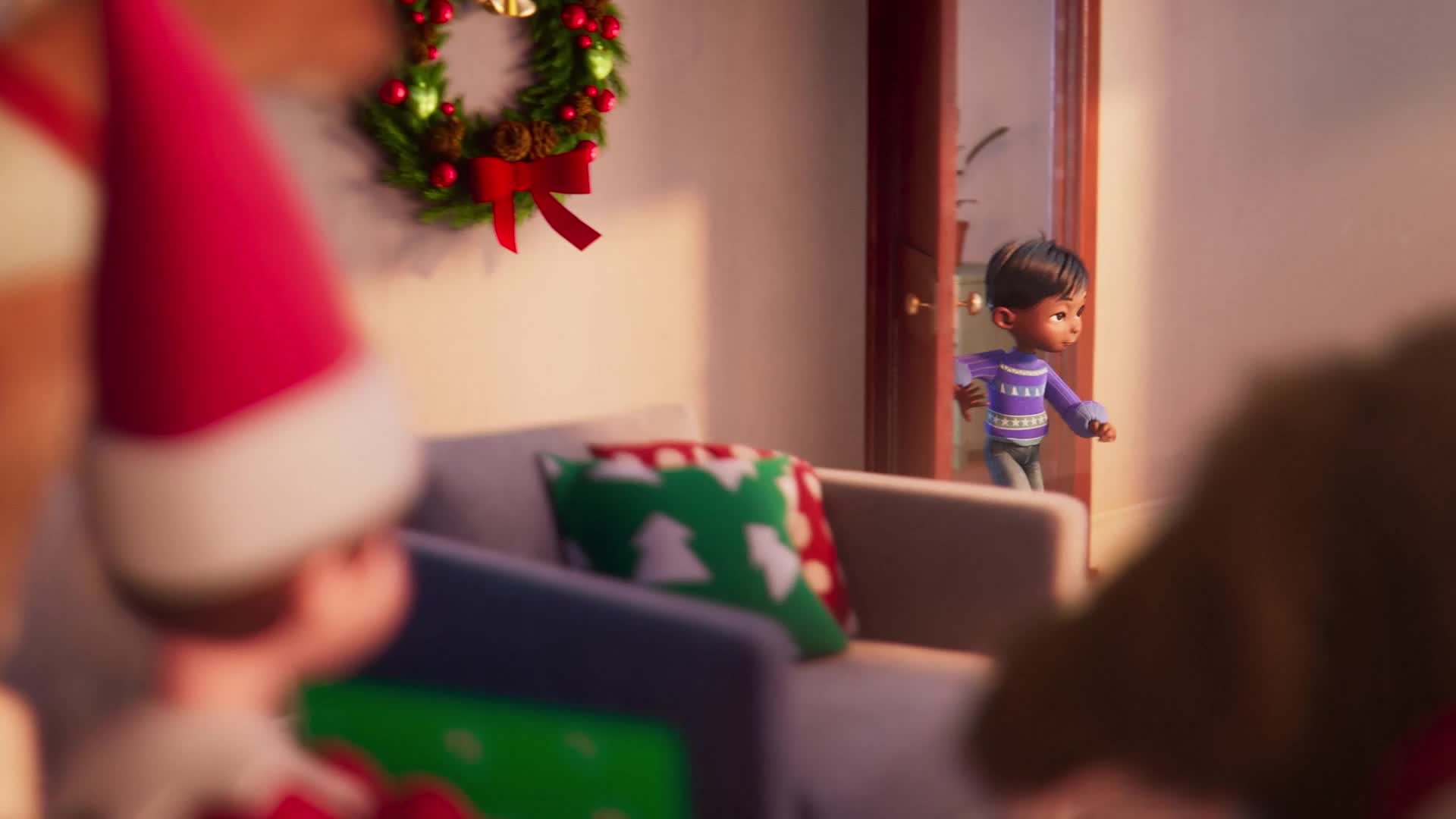 A small boy, wearing a purple sweater, bursts through a doorway. He's heading towards someone wearing a Santa hat, who's sitting on a sofa decorated with festive cushions.
