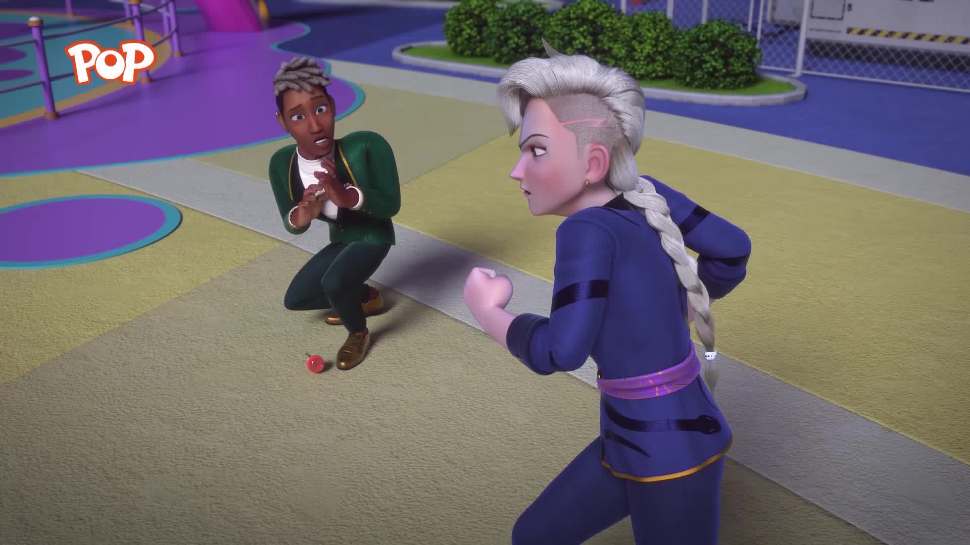 A young man in a green suit crouches, hands clasped in a defensive posture, a small red object at his feet. Across from him, a woman in a blue uniform with a distinctive hairstyle stands ready, her fist clenched.