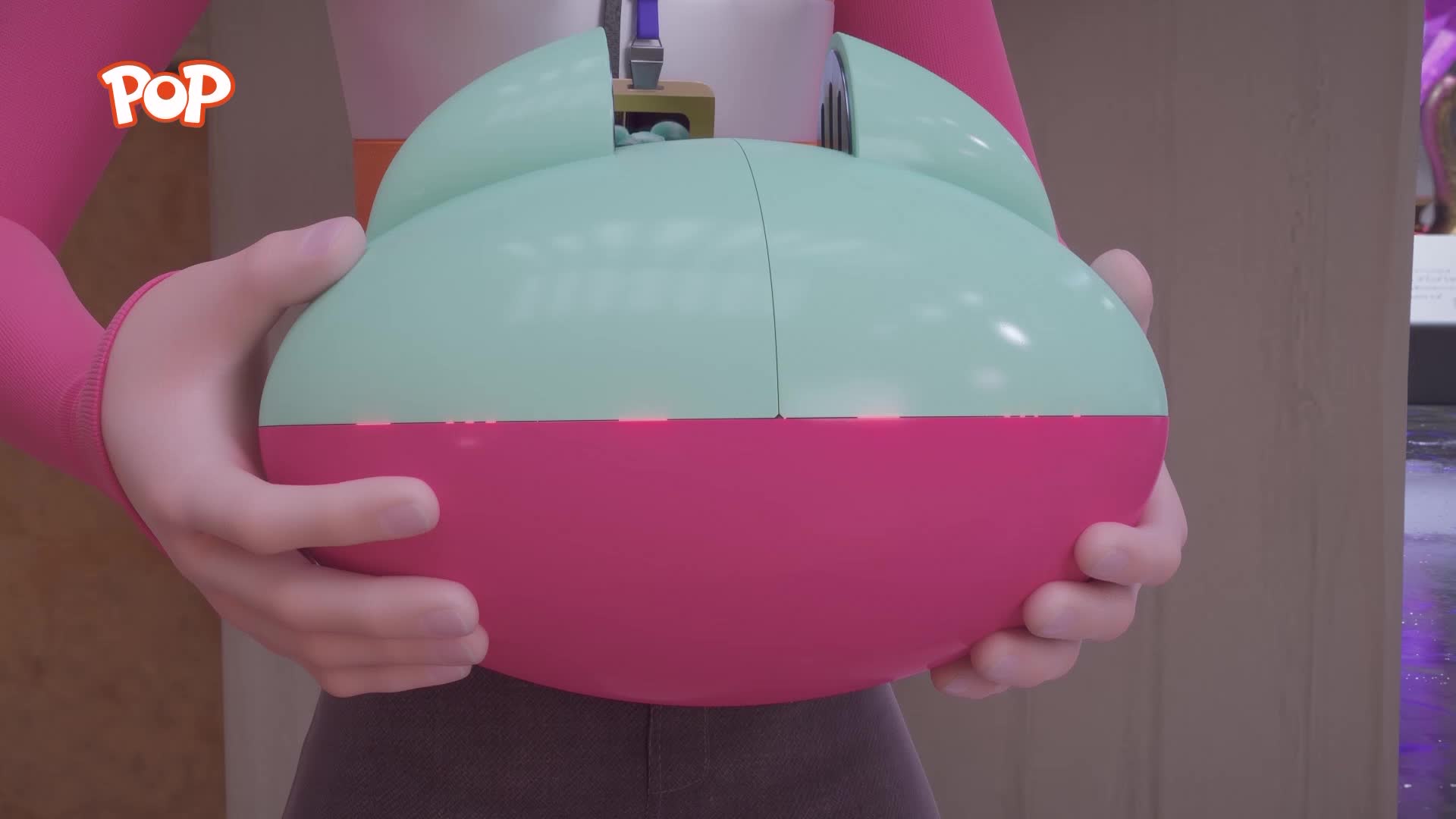A person's hands cradle a round, mint-green and pink object. The object has a small opening at the top, revealing some blue contents.