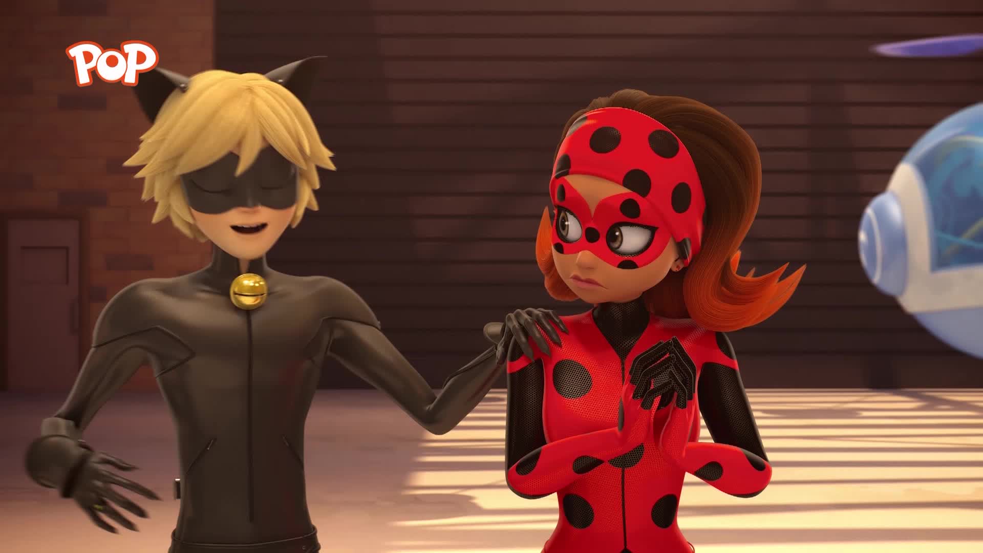 A young man in a black cat suit grins, his hand resting on the shoulder of a girl in a red and black polka-dotted outfit. Behind them, a blue, bulbous object with a propeller sits on the ground.